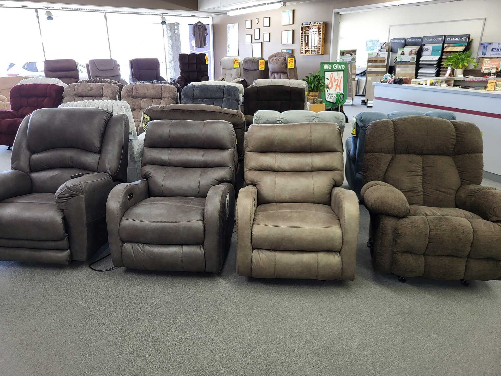 Several upholstered recliners on display in a store, varying in color and style, with a carpeted floor.