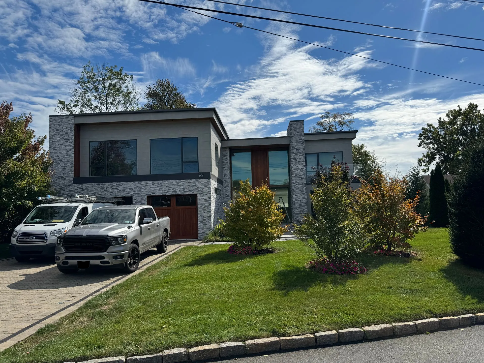 A contemporary two-story house with stone accents, wood garage doors, and large windows, parked with two trucks outside.