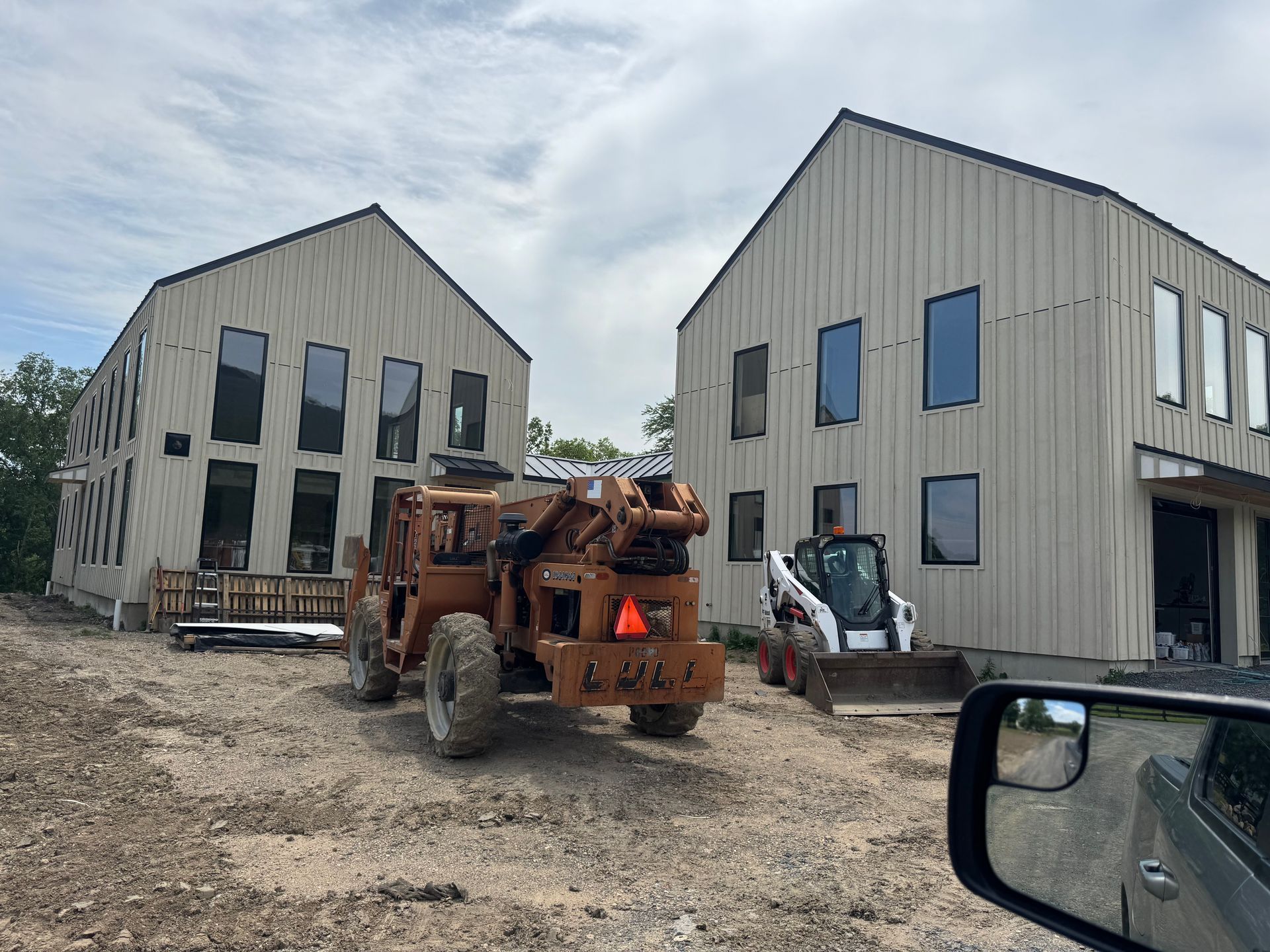 Two beige buildings under construction with a construction lift and a skid steer parked on a gravel lot.