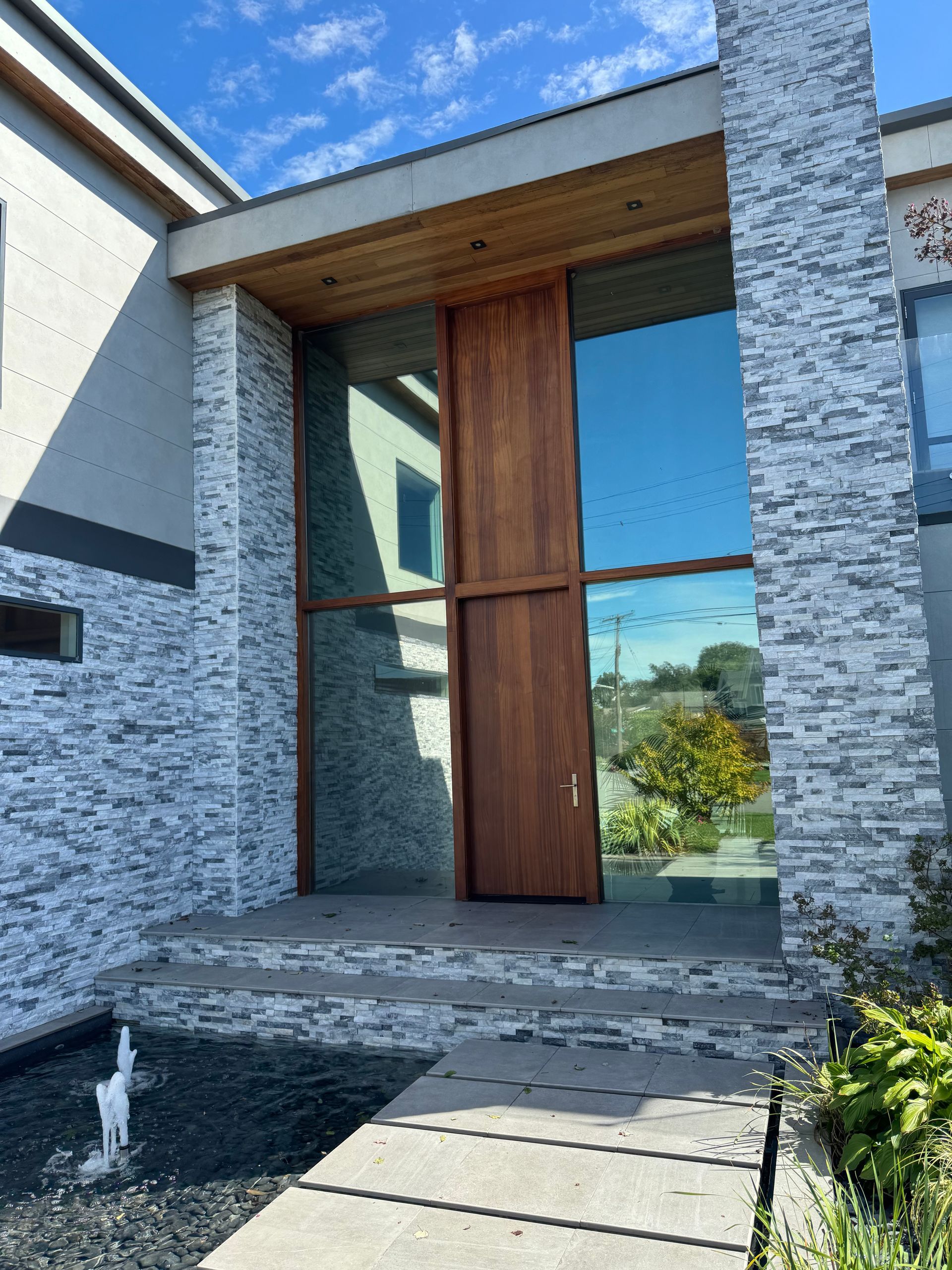 Modern home entrance featuring a tall wood door, large glass panels, and exterior walls clad in gray stacked stone.