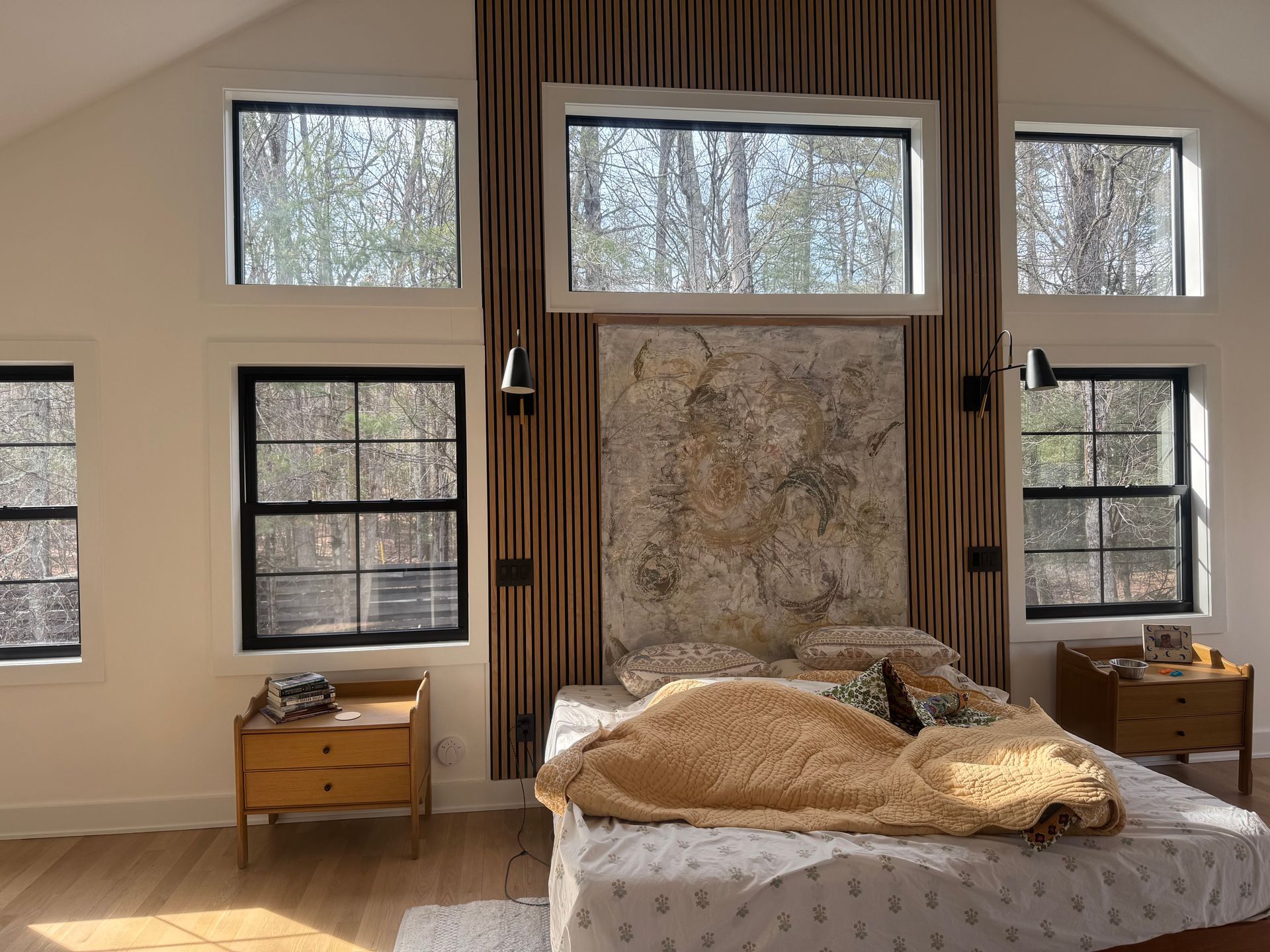 A bright bedroom with a bed centered against vertical wood slats and a map mural between two large black-framed windows.