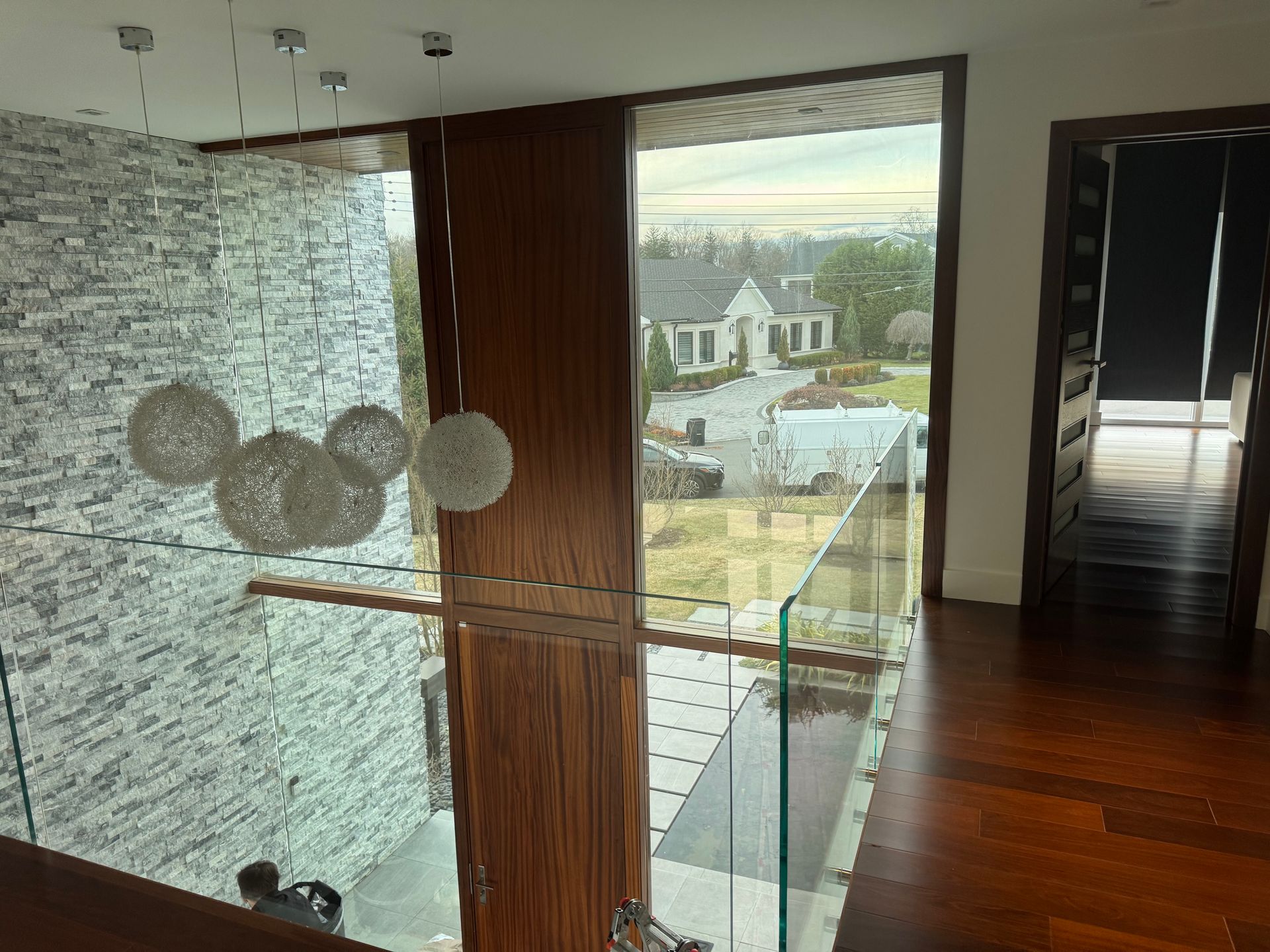 A view from an upper landing featuring a stacked stone wall, modern globe pendant lights, and a glass-paneled railing.