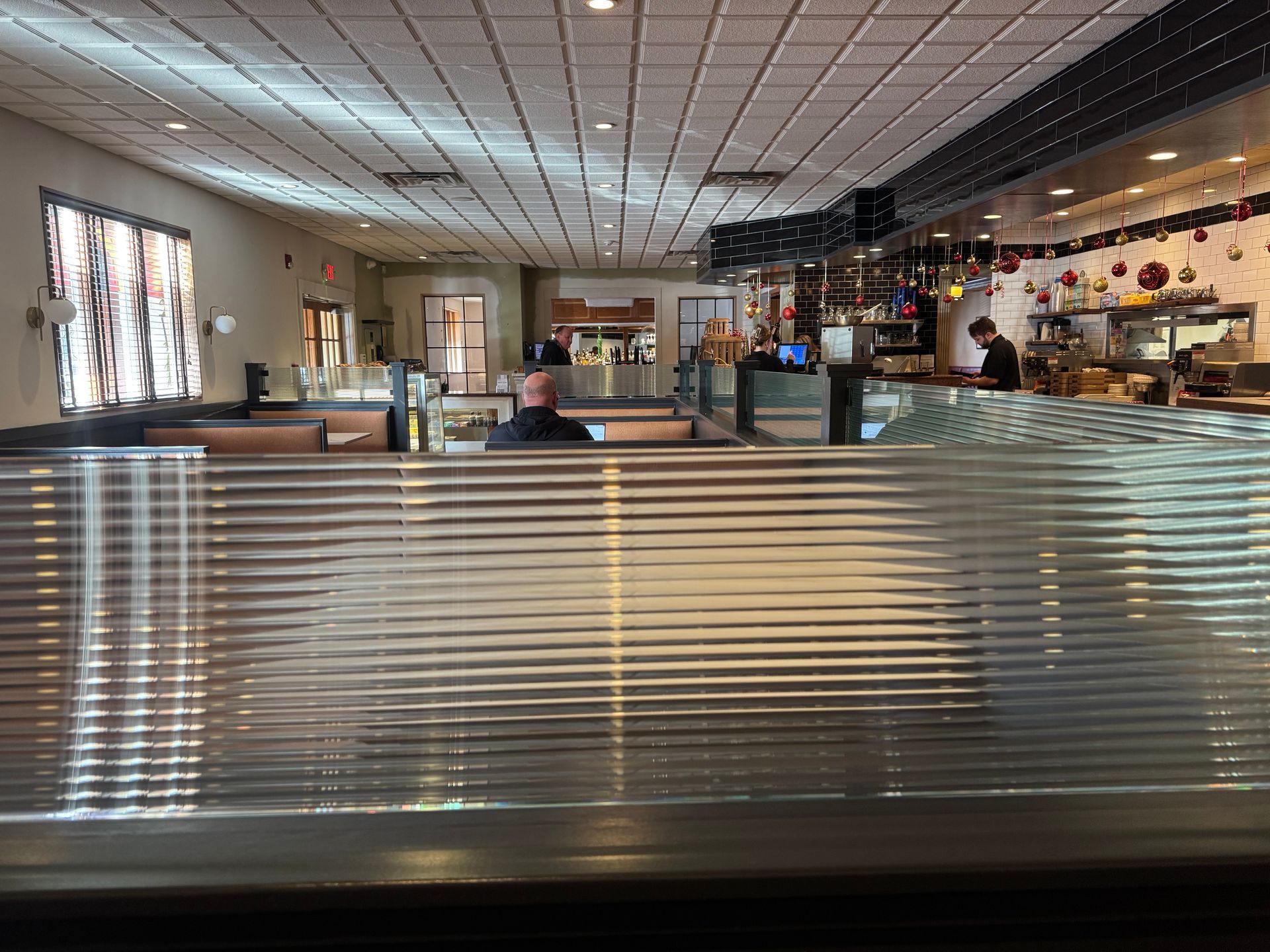 Interior view of a restaurant looking past a textured, ribbed privacy screen toward the counter and seating area.