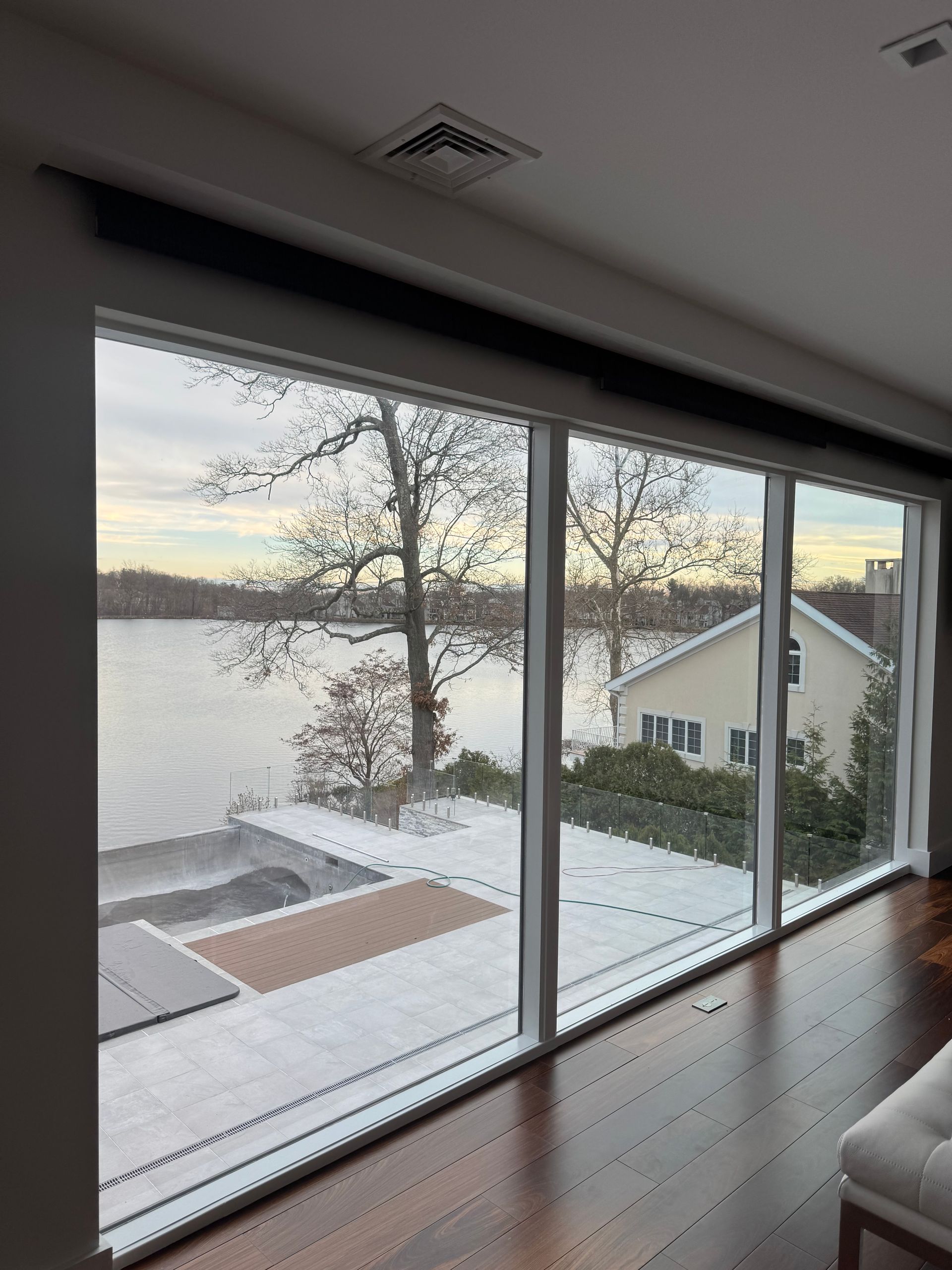 A bright living room with floor-to-ceiling windows overlooking a snowy patio and a frozen lake with a house in distance.
