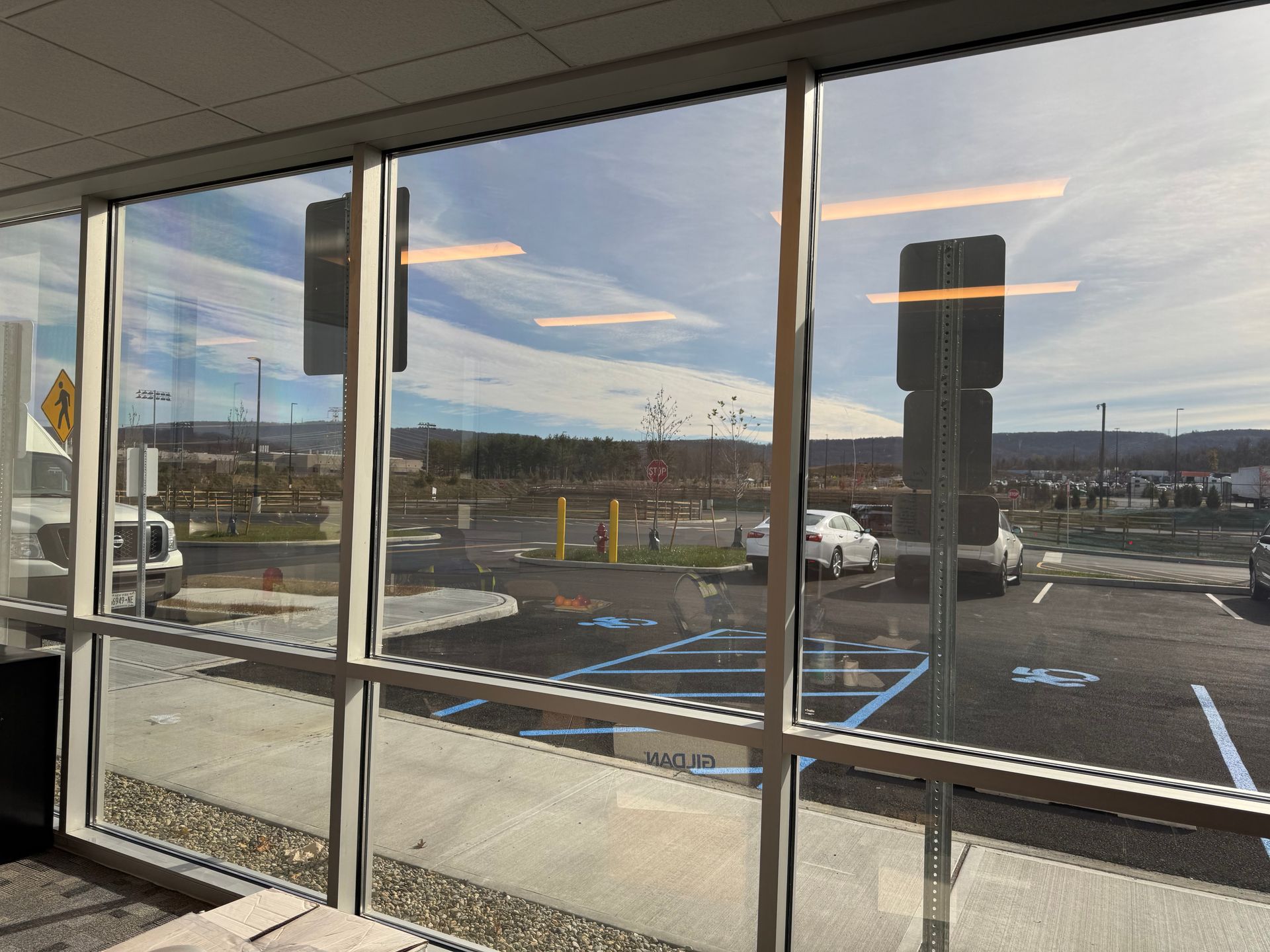 A view through office windows looking out onto a parking lot with marked handicap spaces and a distant hillside.
