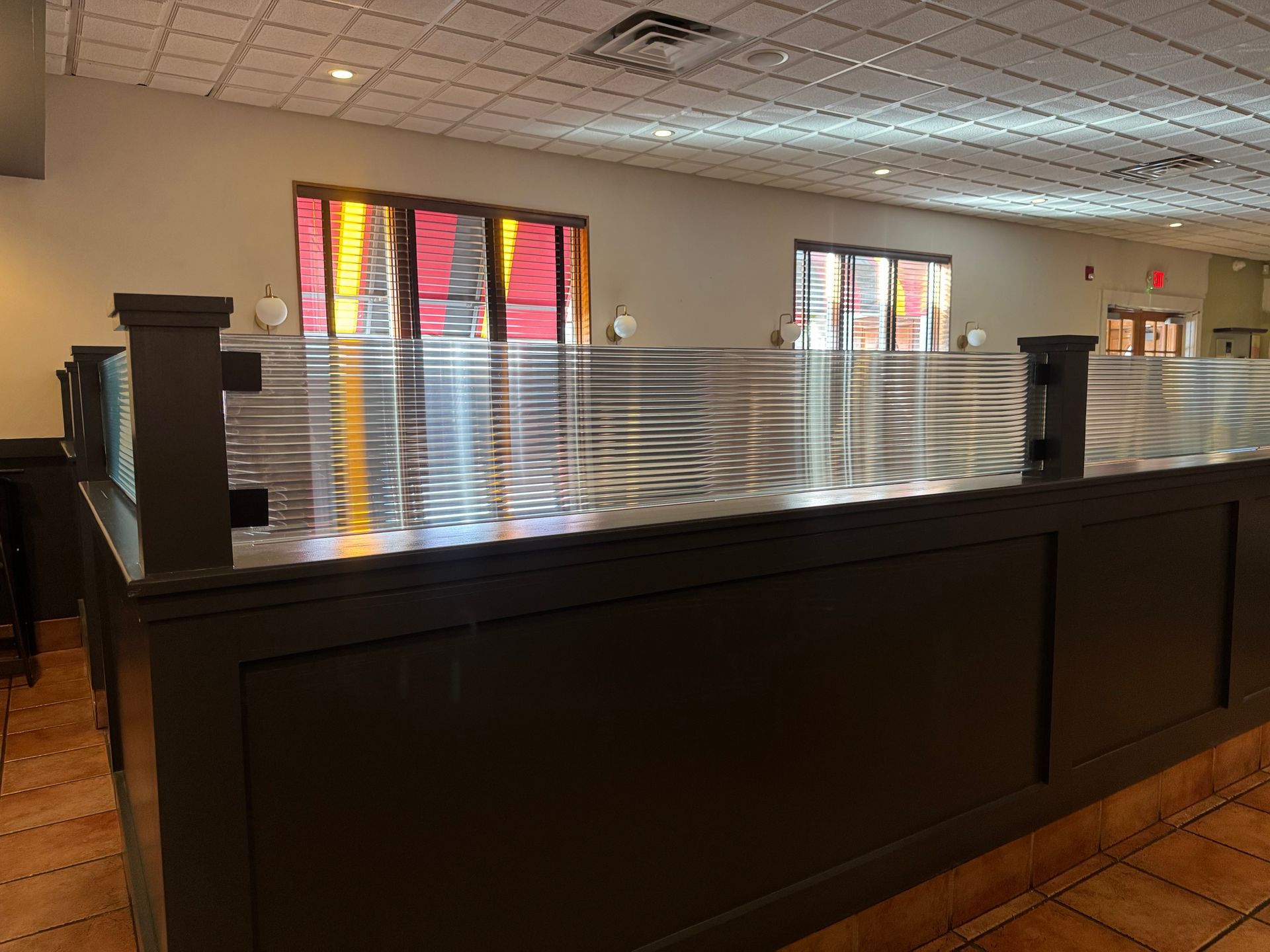 A dark gray restaurant booth divider with a textured, rippled glass upper section in a dining room.