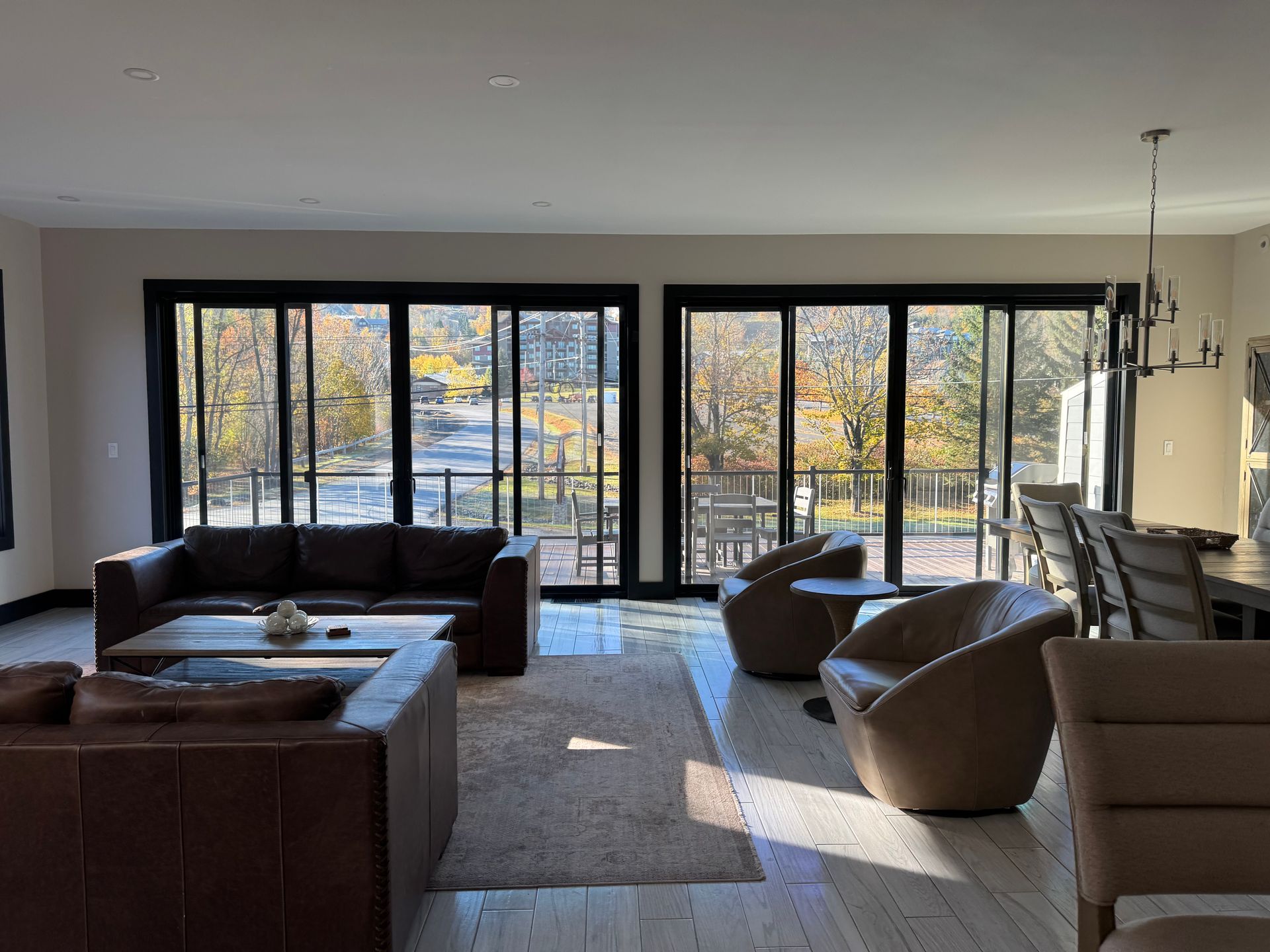 A spacious, modern living room with leather sofas, chairs, a rug, and large windows looking out onto a wooded landscape.