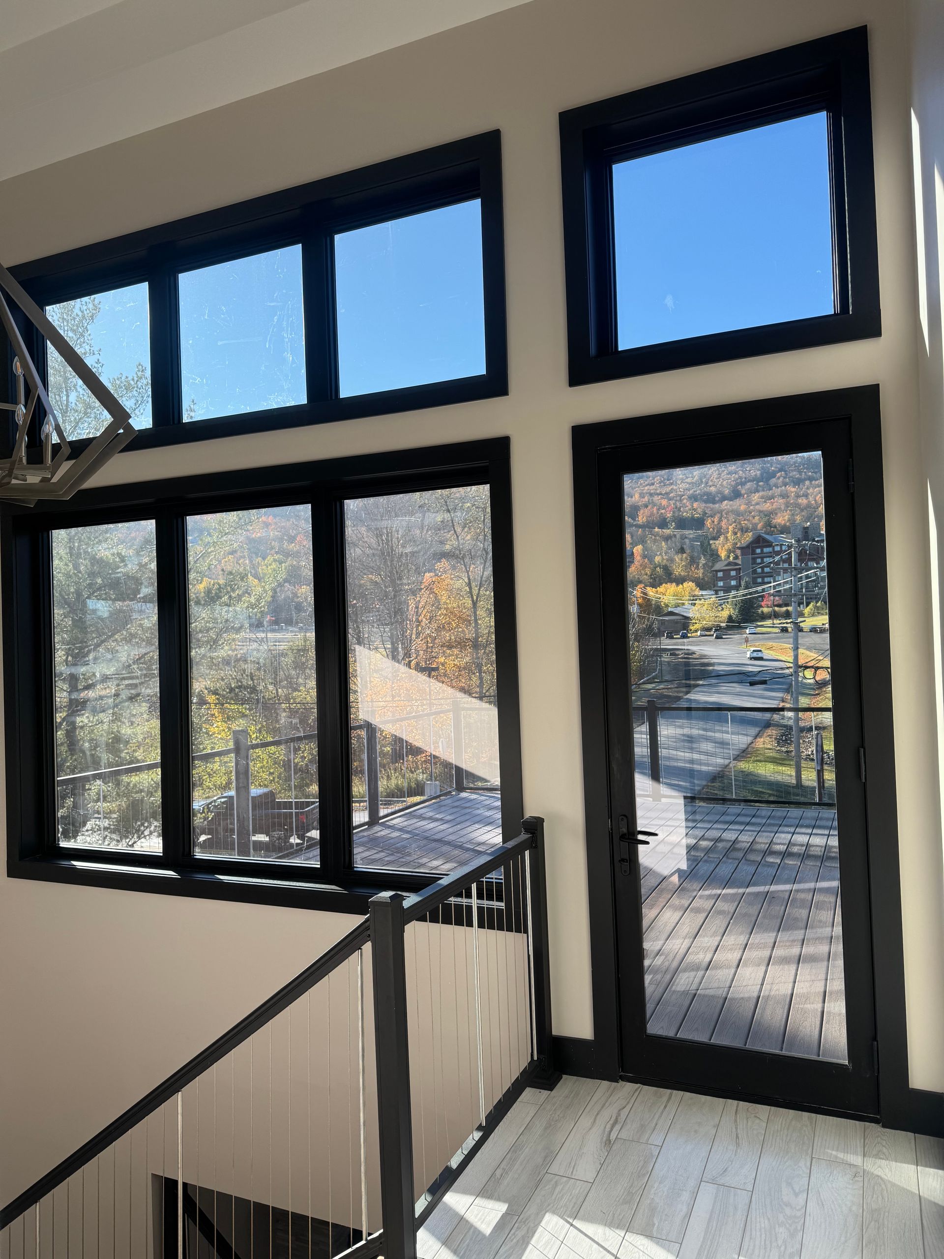 A high-ceilinged room with black-framed windows and a door overlooking a scenic, wooded outdoor landscape.