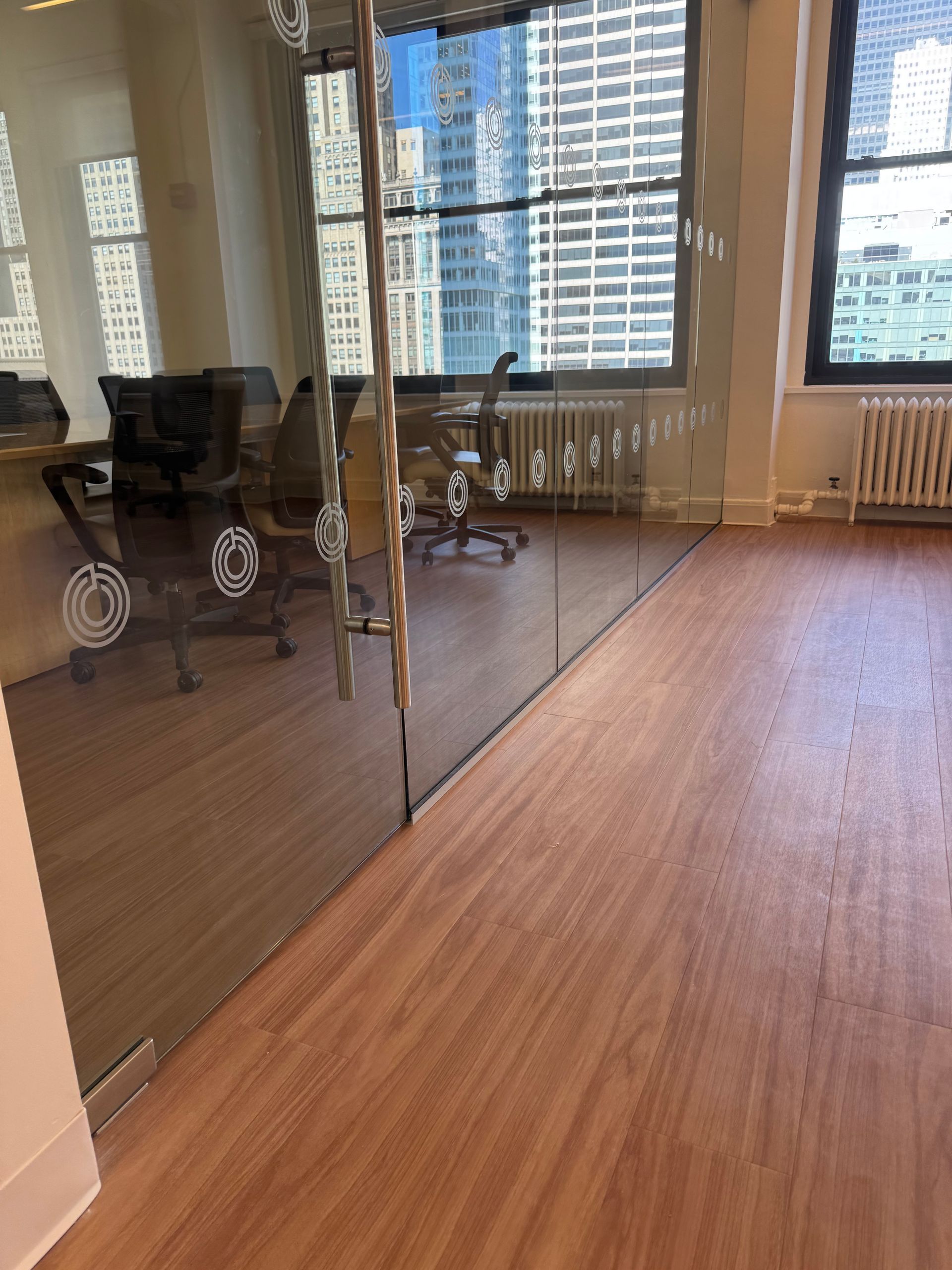A glass-walled conference room with office chairs and a view of city skyscrapers through large windows.