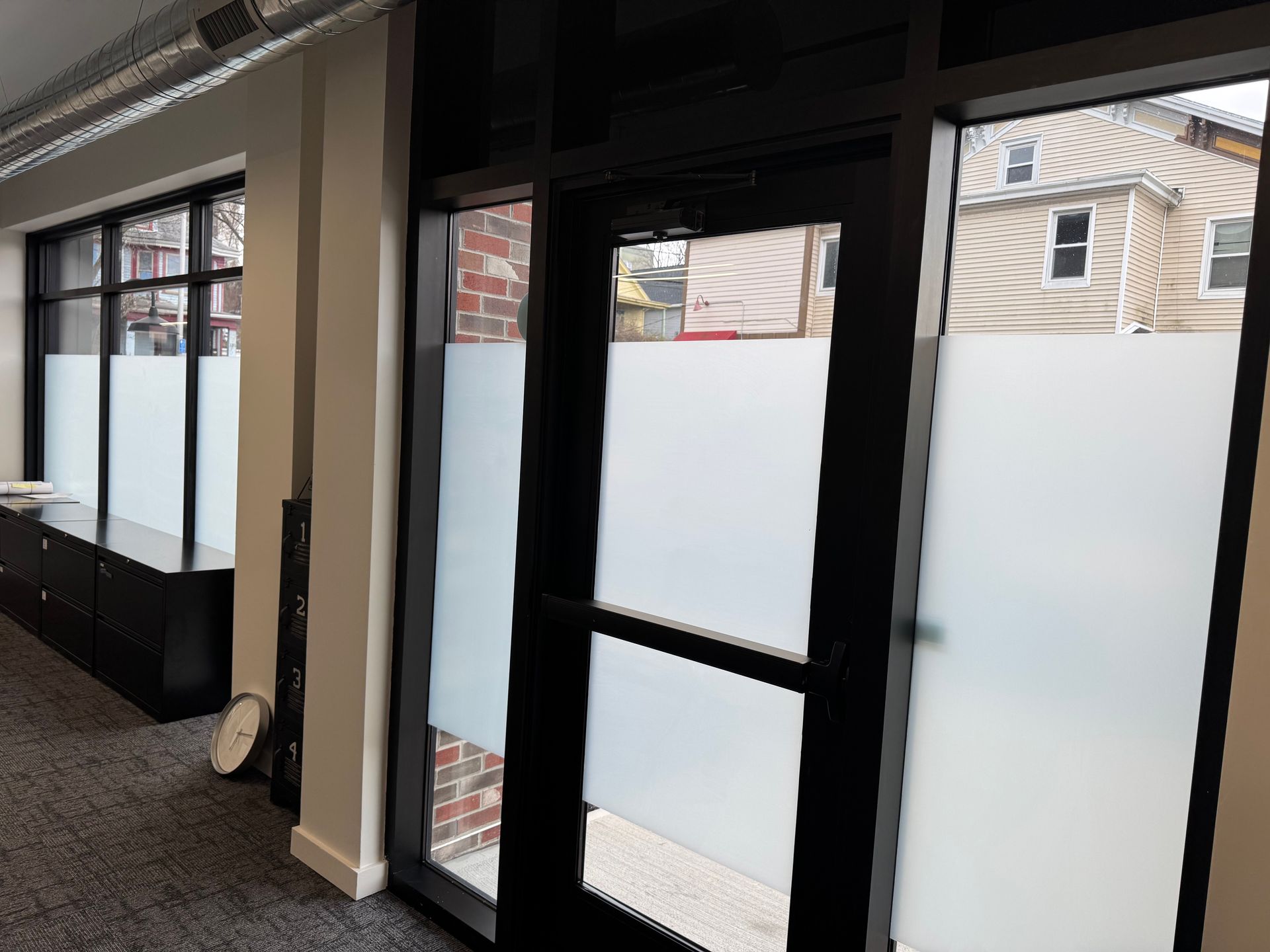 Interior view of an office with large windows and a glass door, featuring frosted privacy film on the lower panels.