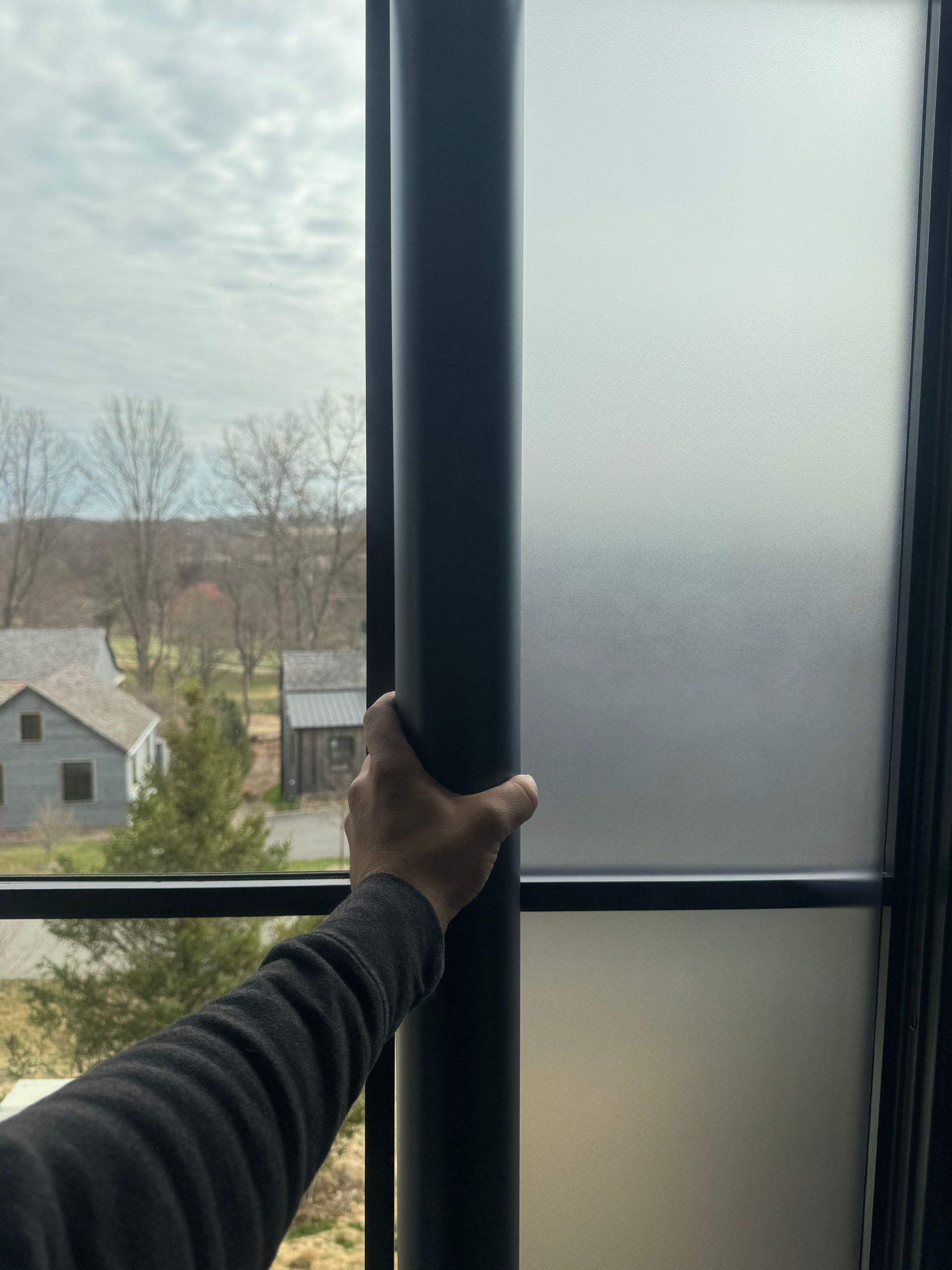 A hand holds a vertical black post in front of a window, which has clear glass on the left and frosted glass on the right.