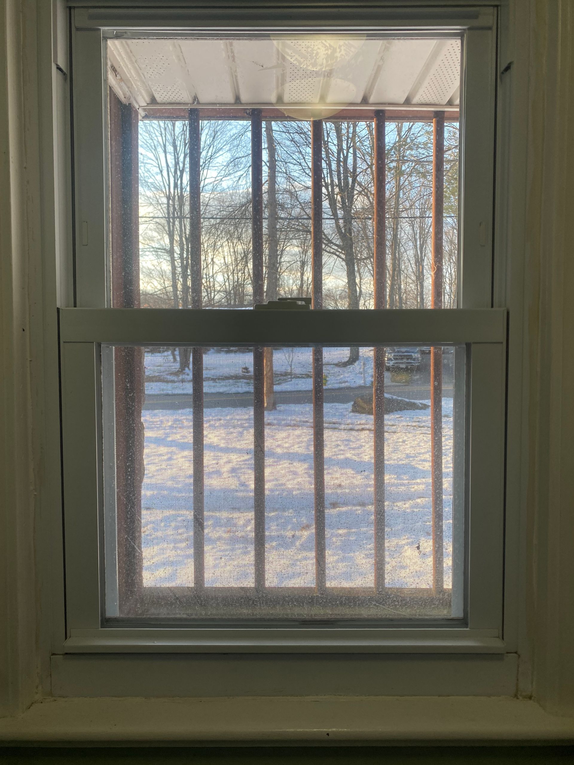 A view through a white-framed window looking out onto a snowy yard with a wooden porch structure in the foreground.