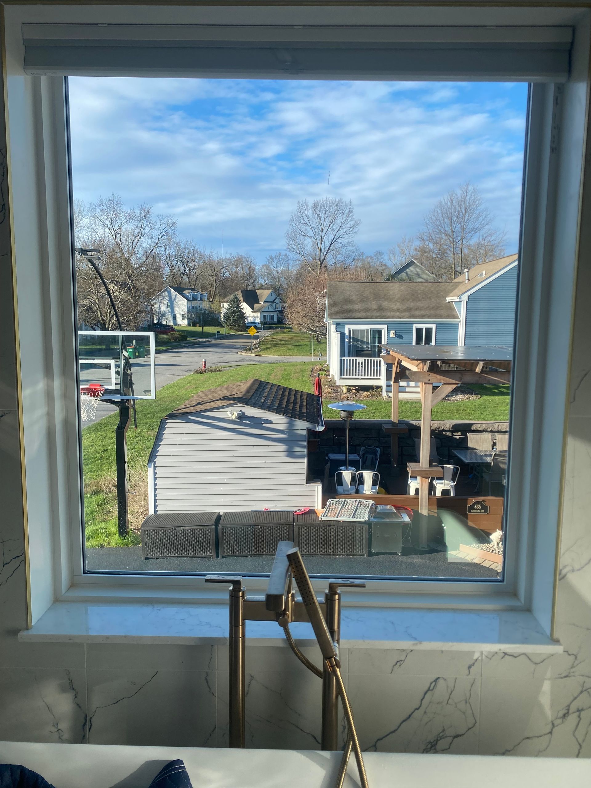 A view through a window in a bathroom looking out over a backyard with a shed, a gazebo, and a basketball hoop.