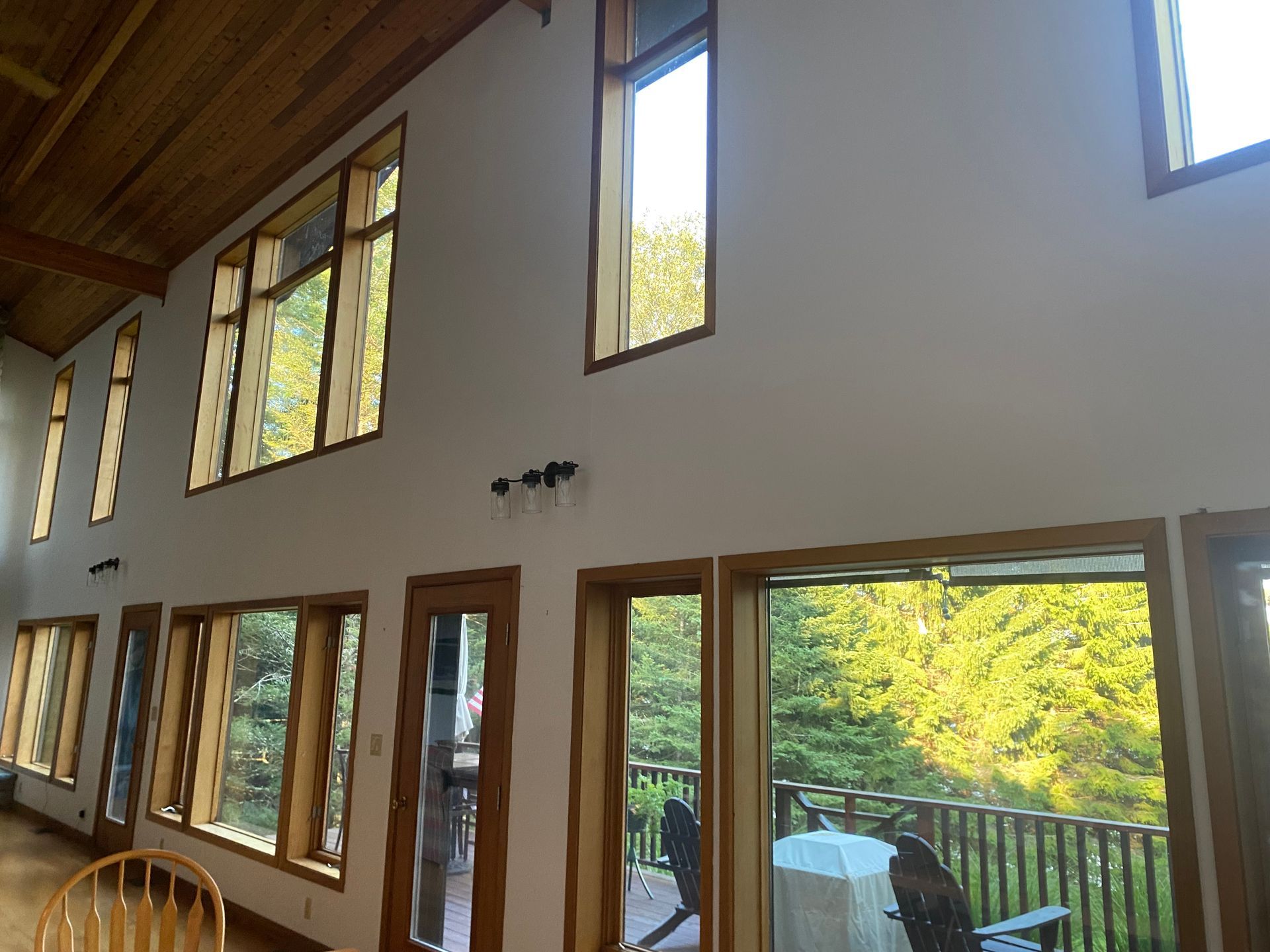 A high-ceilinged room with light walls, wood-trimmed windows, a wooden ceiling, and views of a lush green outdoor area.