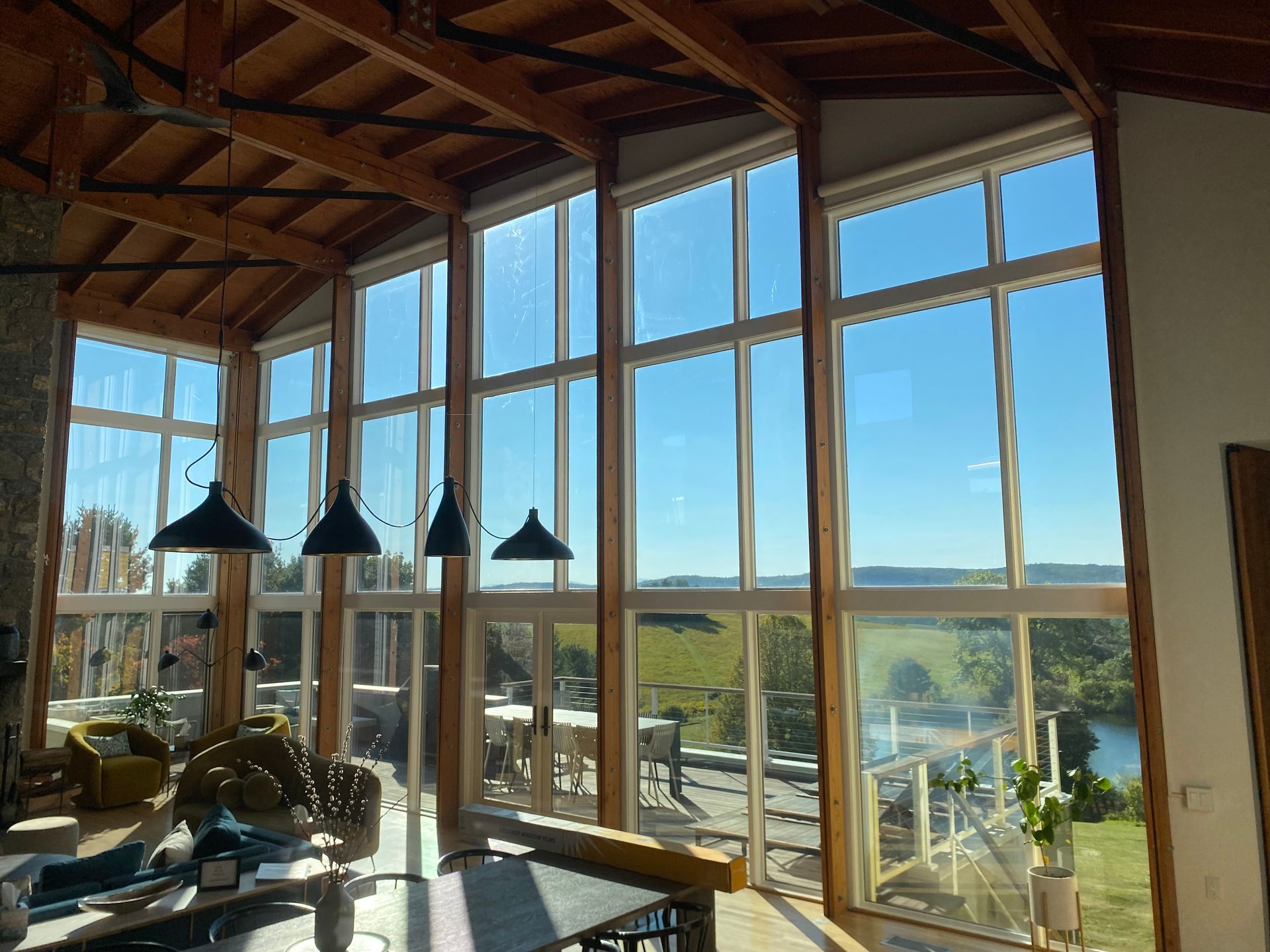 A spacious room with floor-to-ceiling windows, wooden rafters, hanging pendant lights, and a view of a sunny landscape.