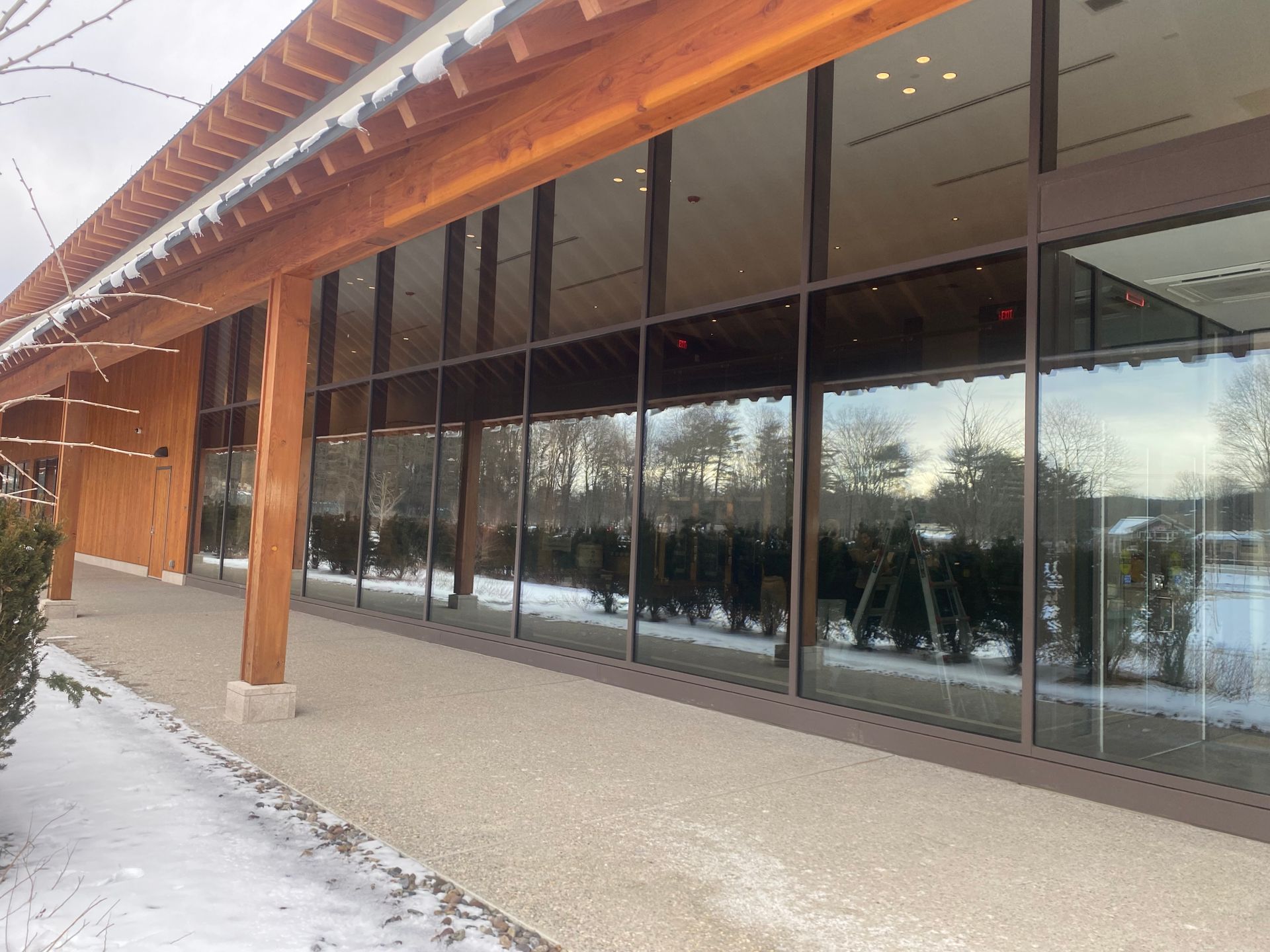 A wooden-framed building with floor-to-ceiling glass windows overlooking a snowy, tree-lined path.