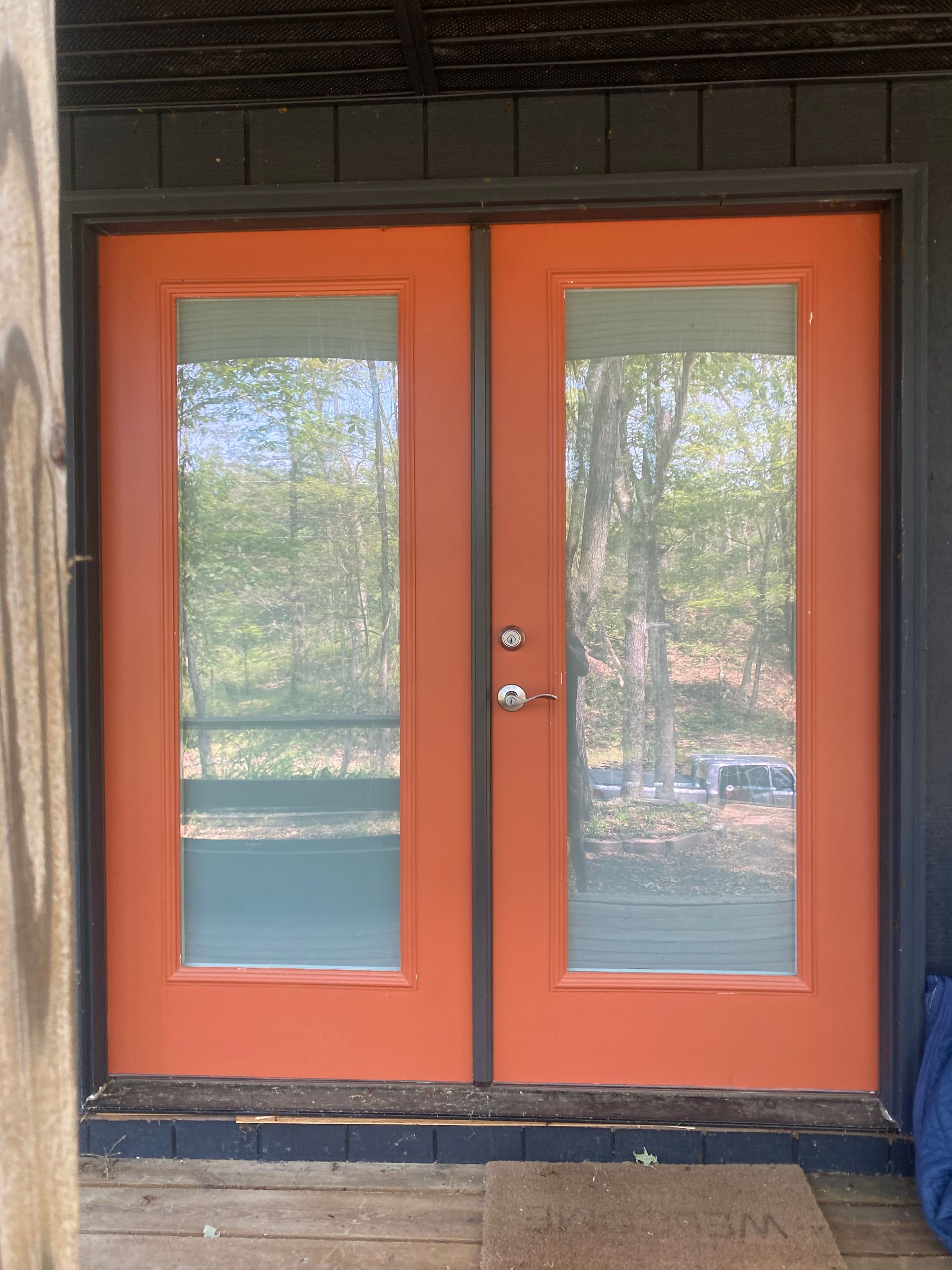 Bright orange double doors with large glass panes, framed in dark trim, set against a dark exterior wall.