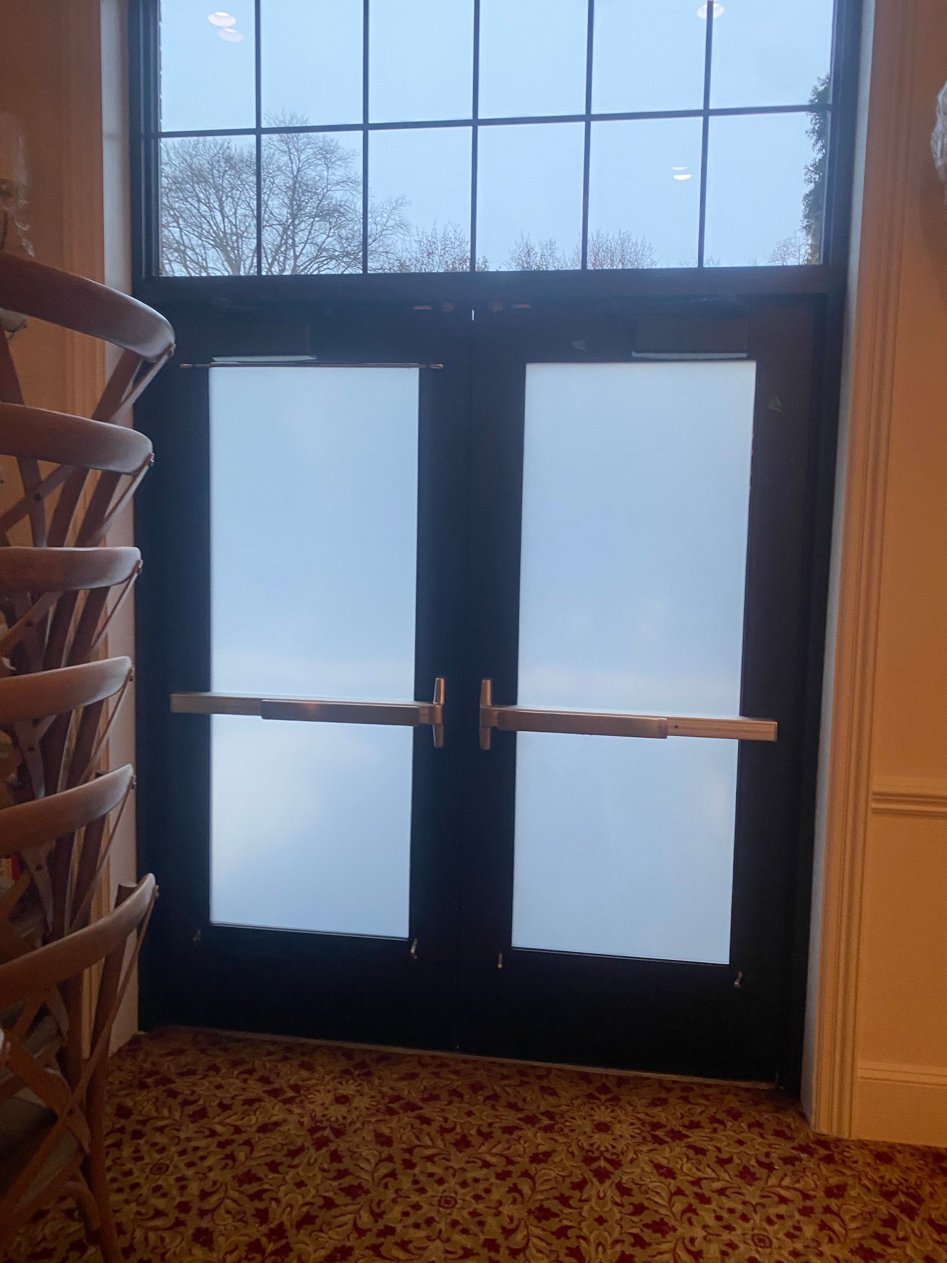 A pair of black double doors with frosted glass panels and horizontal push-bar handles inside a room with patterned carpet.