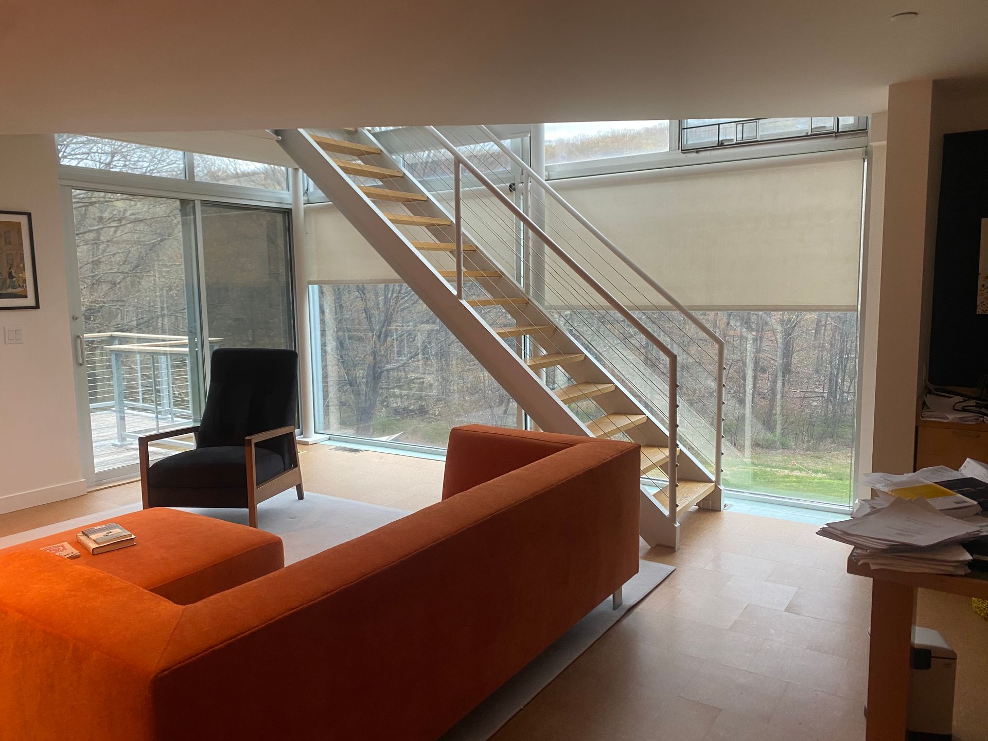 Modern living room with a bright orange sectional, black armchair, and wooden staircase leading to an upper level.