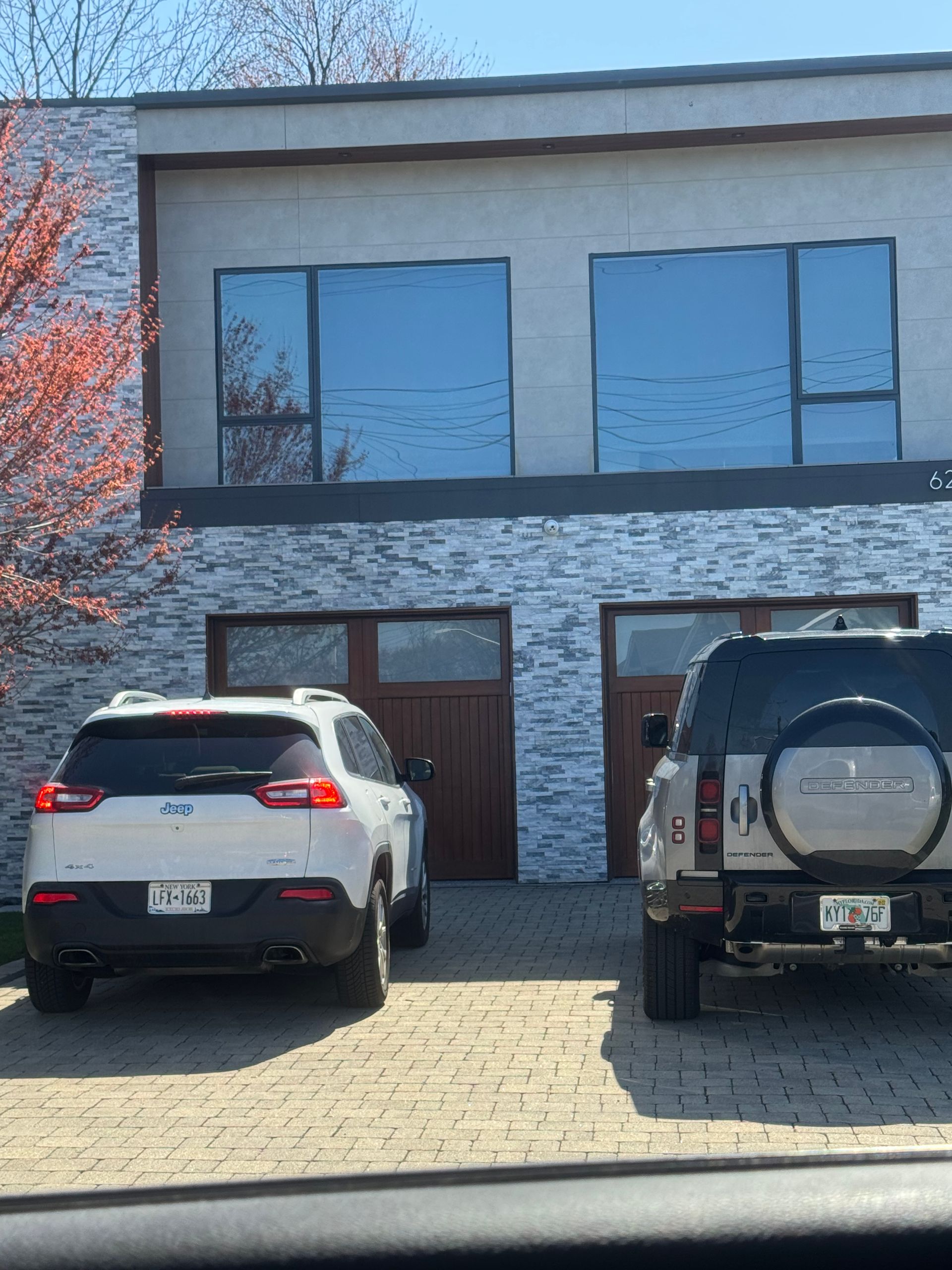A white SUV and a dark grey SUV parked on a paved driveway in front of a modern home with stone siding.