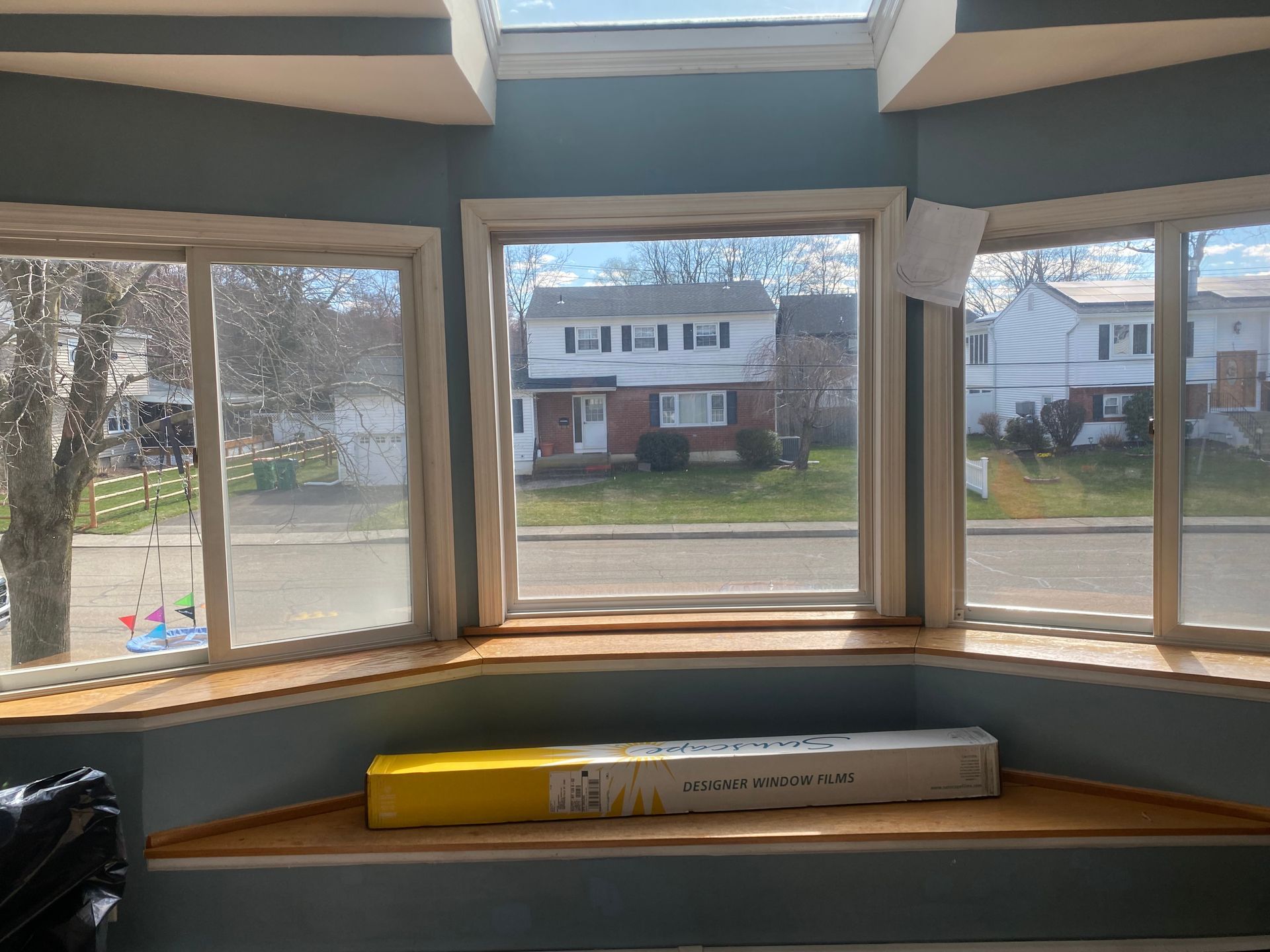 A sunroom with a bay window overlooking a neighborhood street, featuring a wooden ledge and a box on the window seat.