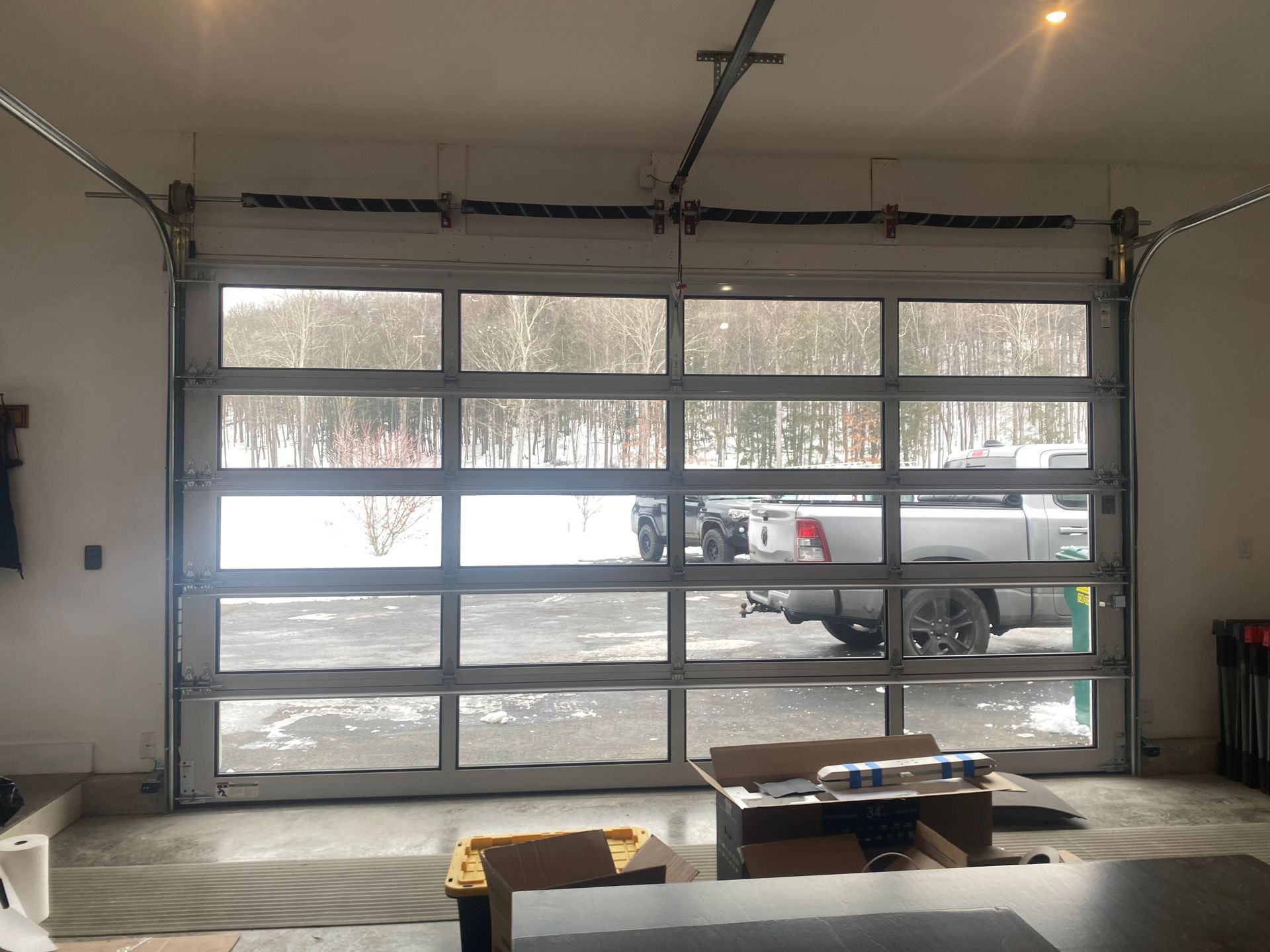 A modern glass-paneled garage door opens to show a snowy outdoor scene with a parked truck in a driveway.