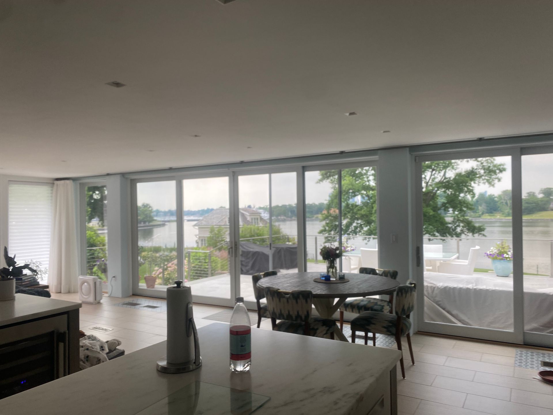 A bright, modern kitchen looking out through large glass sliding doors at a serene lake view with trees and a patio.
