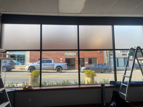A street view through four large, frosted office windows, with construction ladders visible on both sides of the frame.