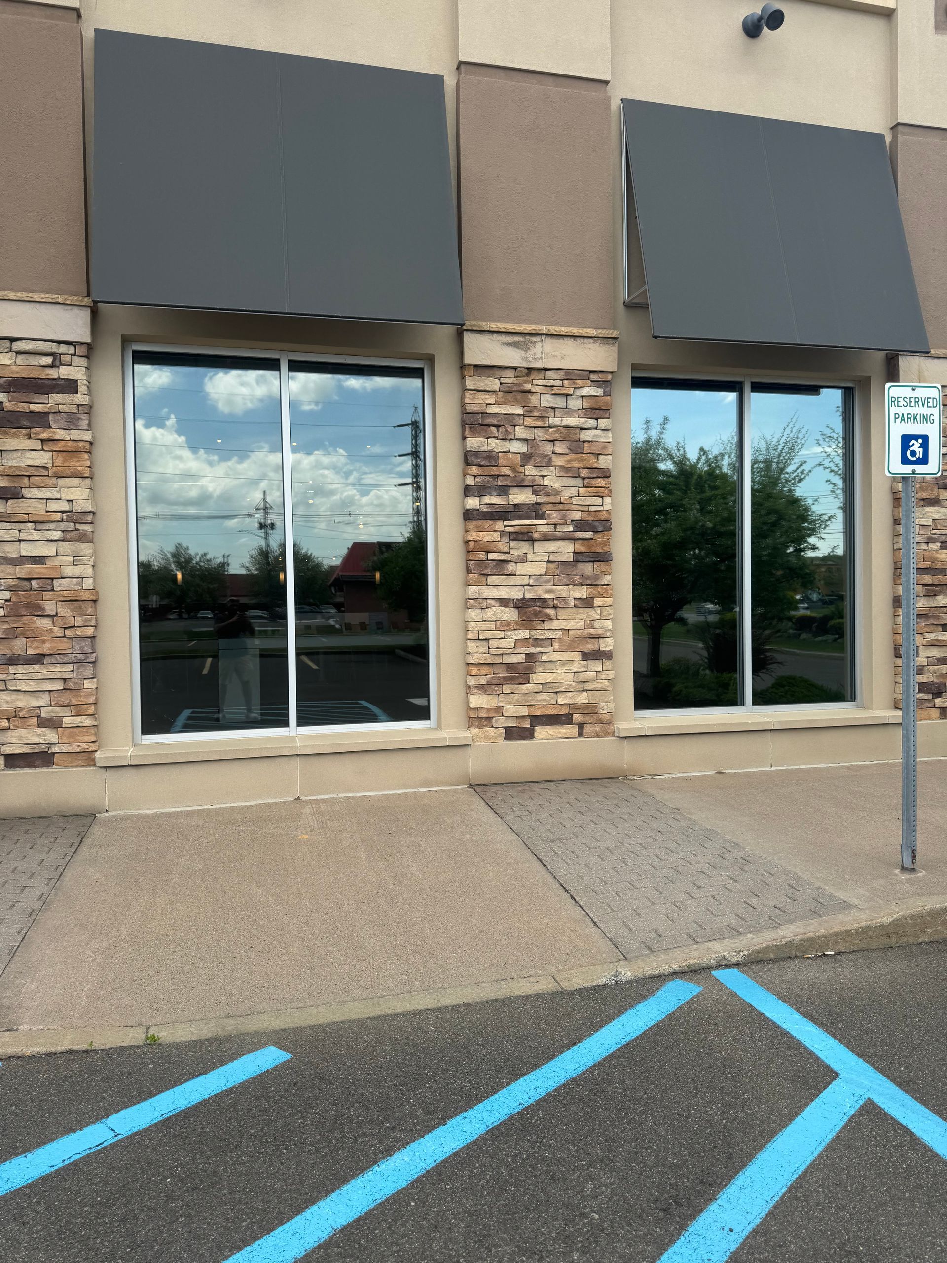 Exterior of a building with two large windows, gray awnings, stone accents, and a blue-marked handicap parking space.