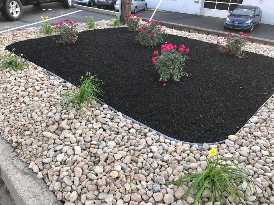 A garden filled with rocks and flowers with a car parked in the background.