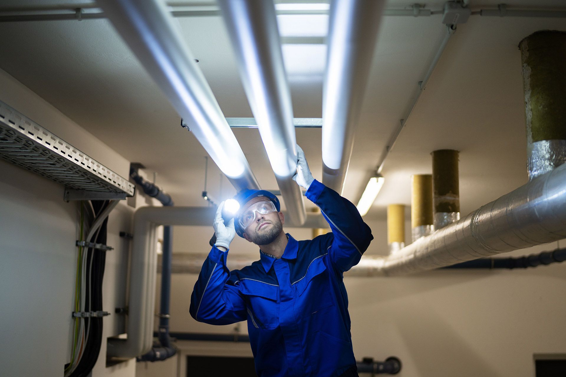 A man is inspecting on a pipe with a flashlight.