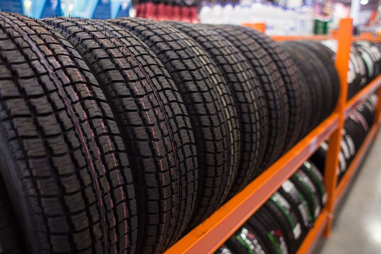 Row of new car tires on an orange shelf in a store.