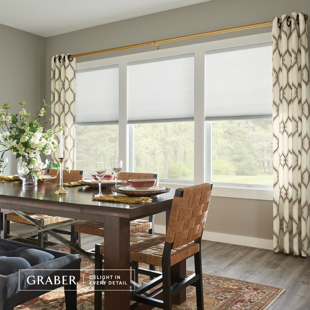Dining room with a table set for a meal, a window with blinds, and patterned curtains.