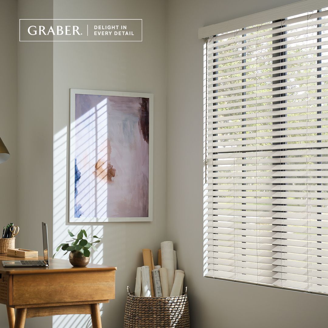 Office space with wooden desk, artwork, and window with blinds. Sunlight streams through.