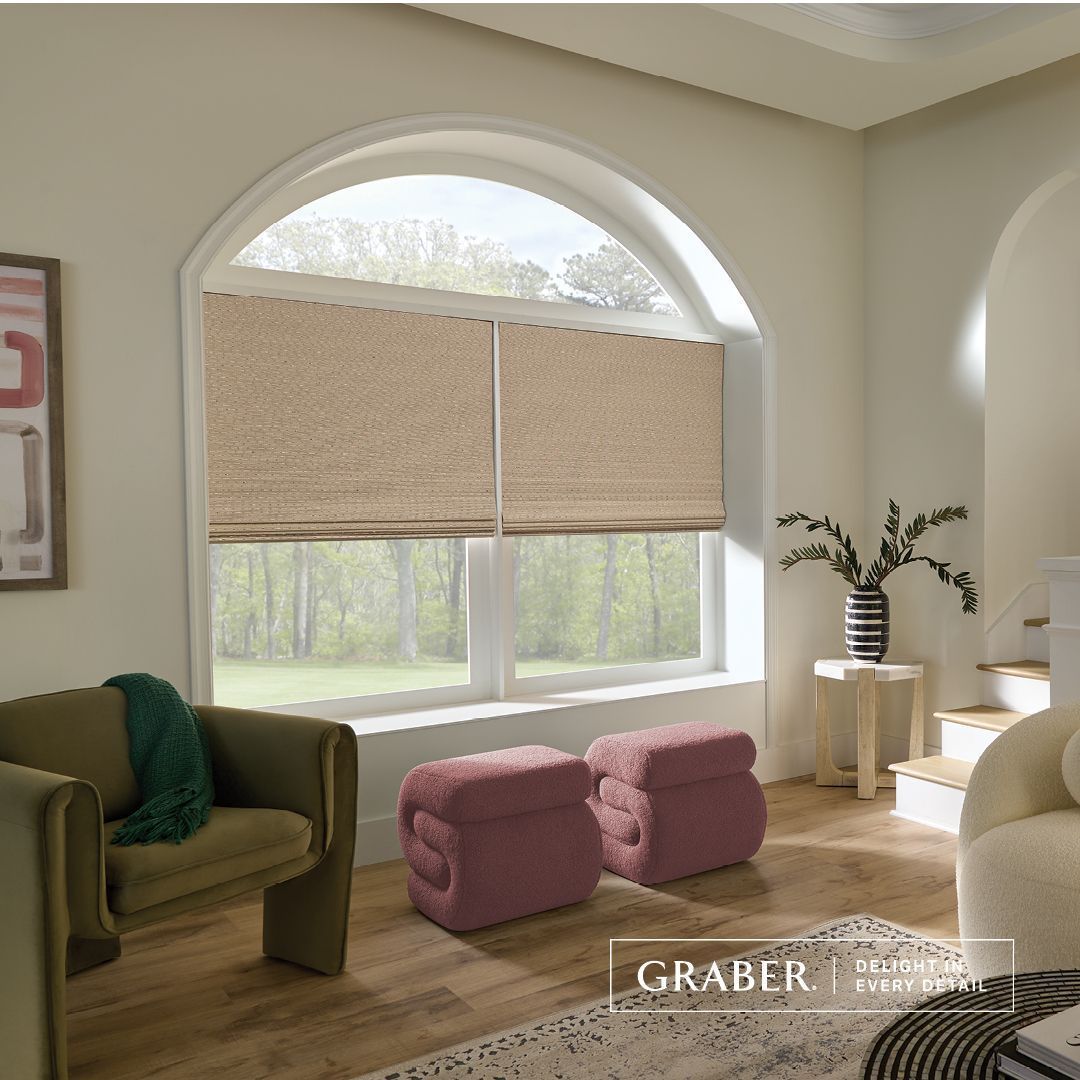 Living room with arched window, shades, green chair, pink ottomans, and small table.