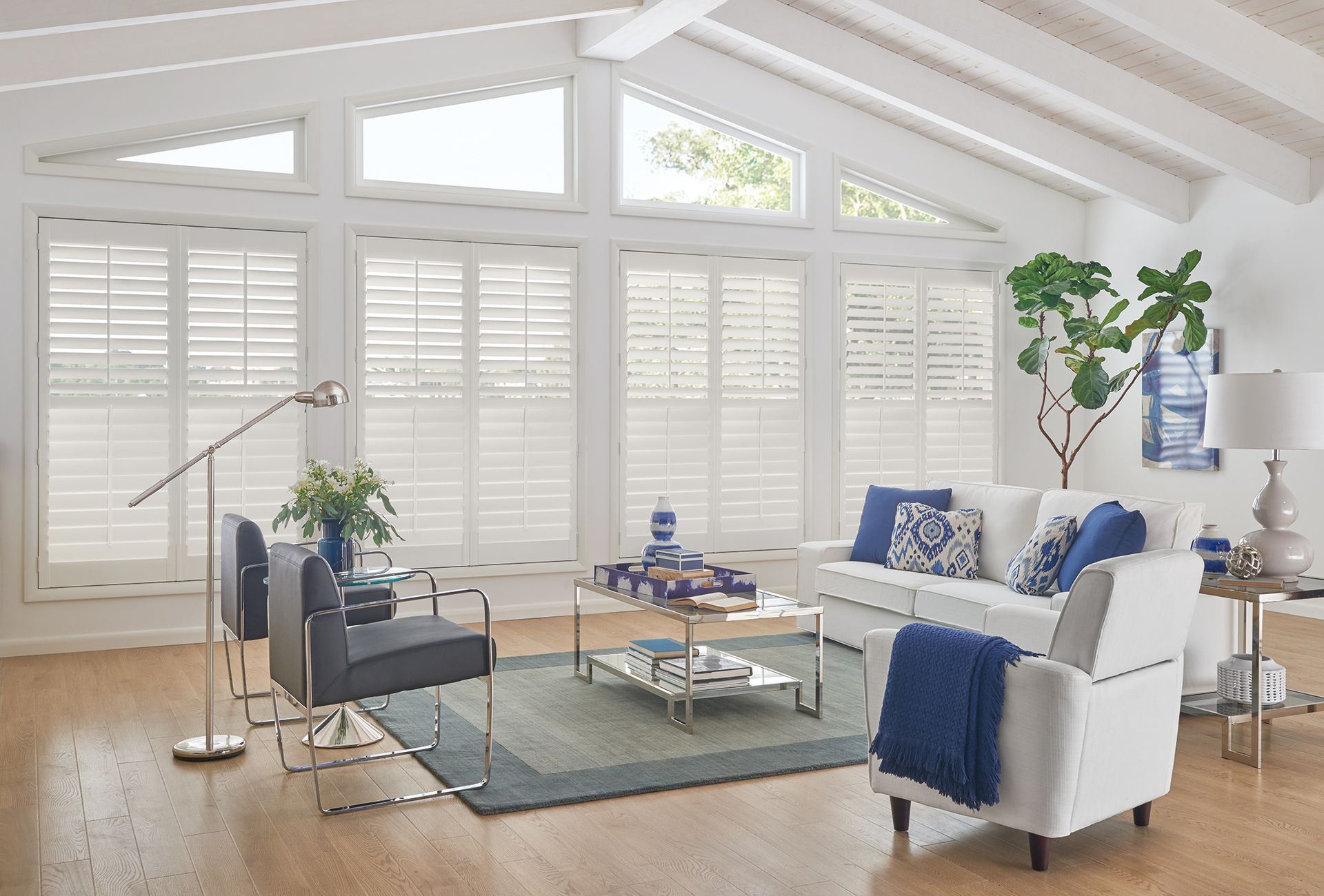 Living room with white shutters, vaulted ceiling, white furniture, blue accents, and hardwood floor.