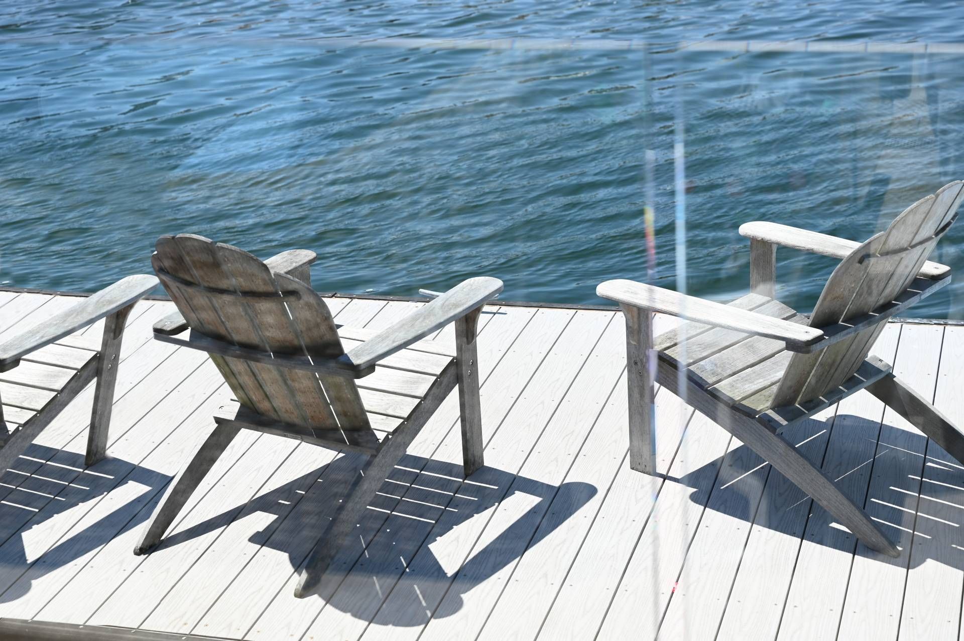 Wooden Adirondack chairs on a dock overlooking a body of water on a sunny day.