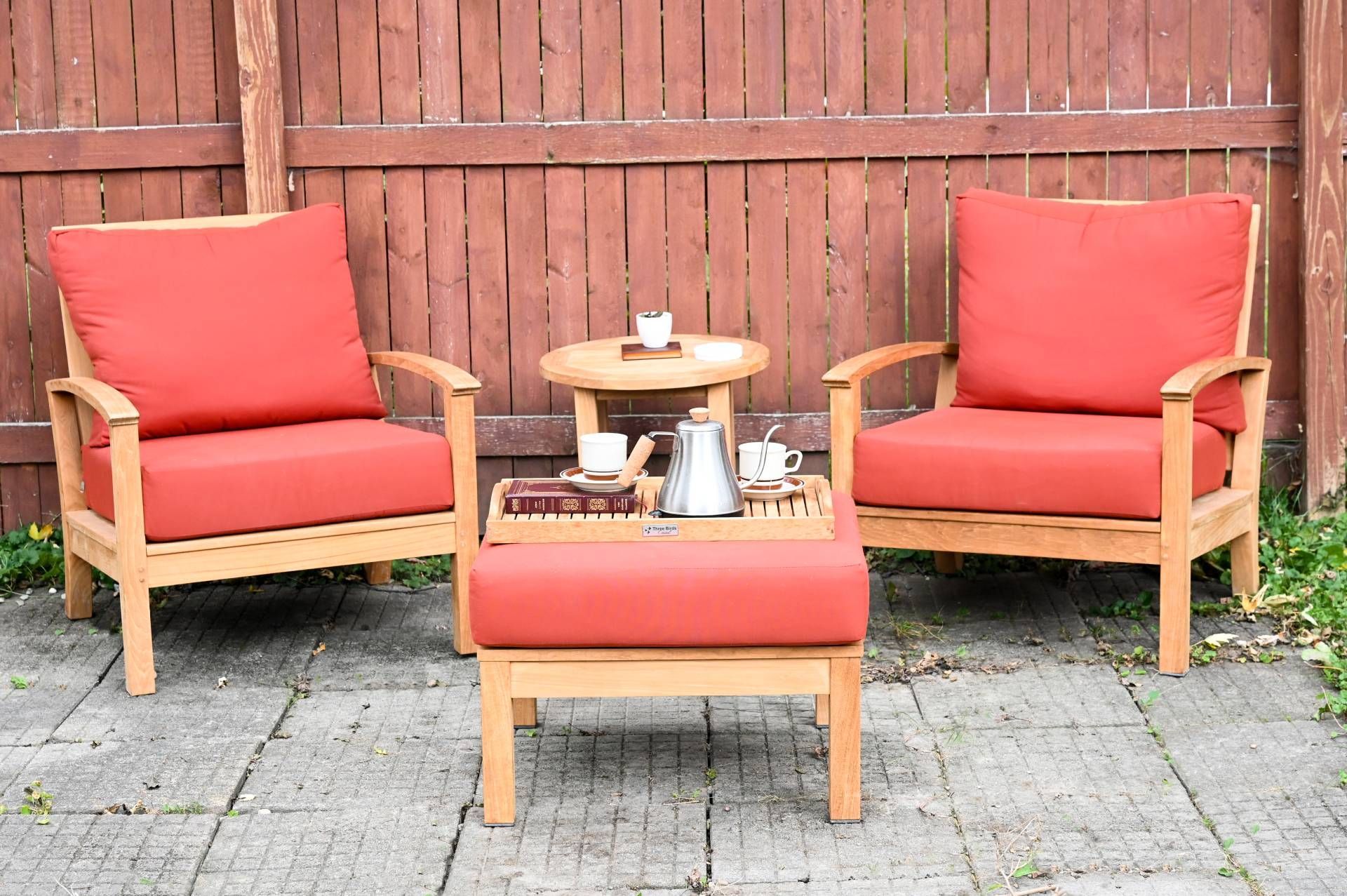 Outdoor seating set with coral cushions on a stone patio against a brown wooden fence.