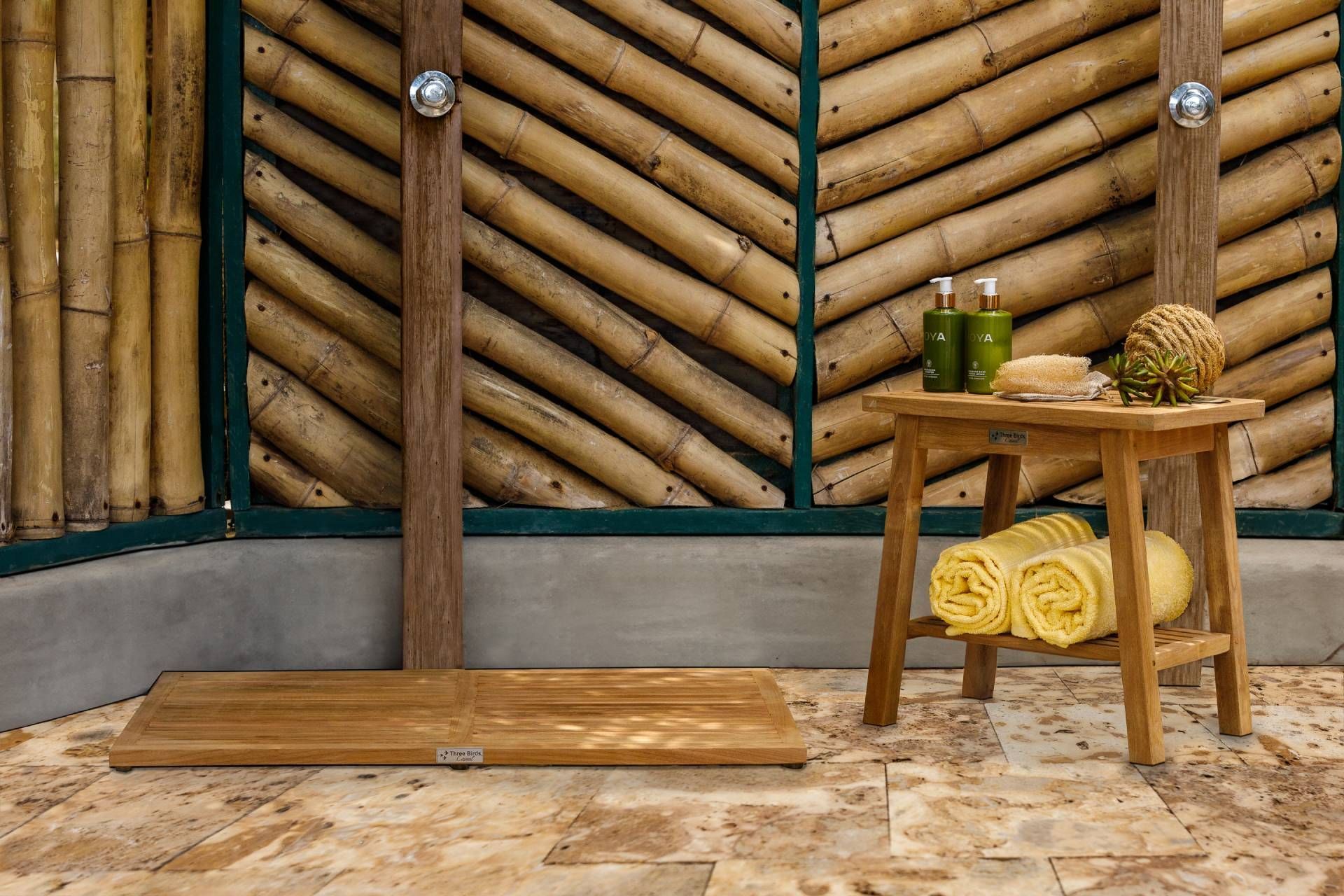 Outdoor shower with bamboo wall, wooden stool holding toiletries and towels.