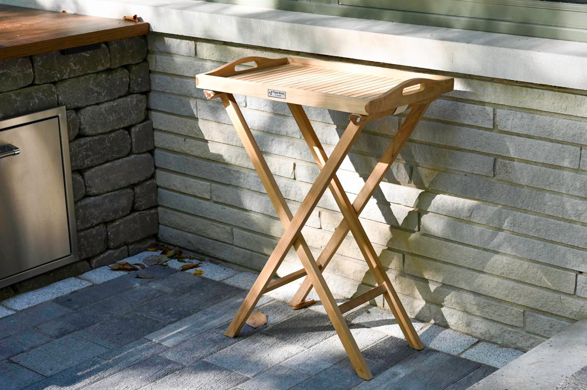 Wooden folding tray table on patio next to a stone wall.