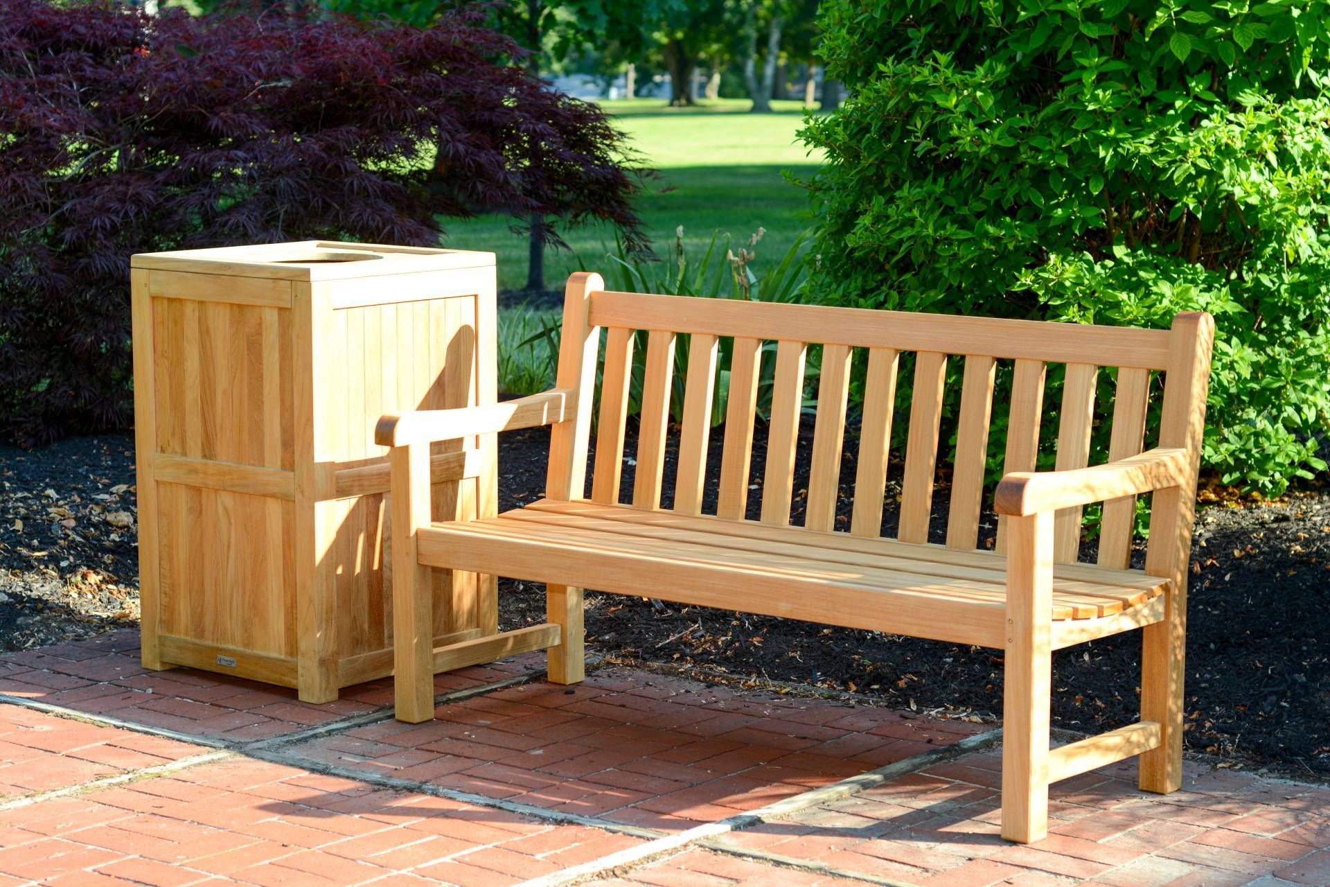 Wooden bench and waste receptacle on a brick patio, near foliage.