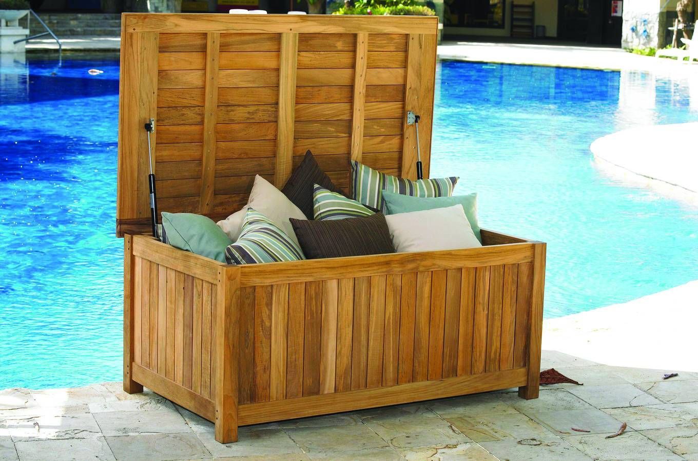 Wooden storage chest with open lid, containing pillows, by a pool.