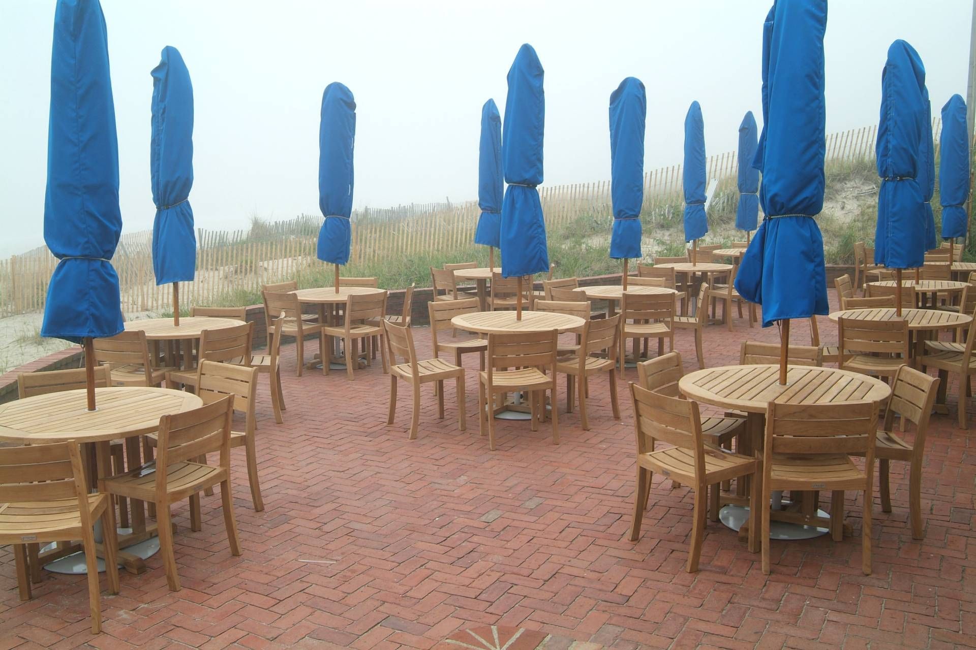 Outdoor restaurant patio with tables, chairs, and blue umbrellas, on a foggy day.