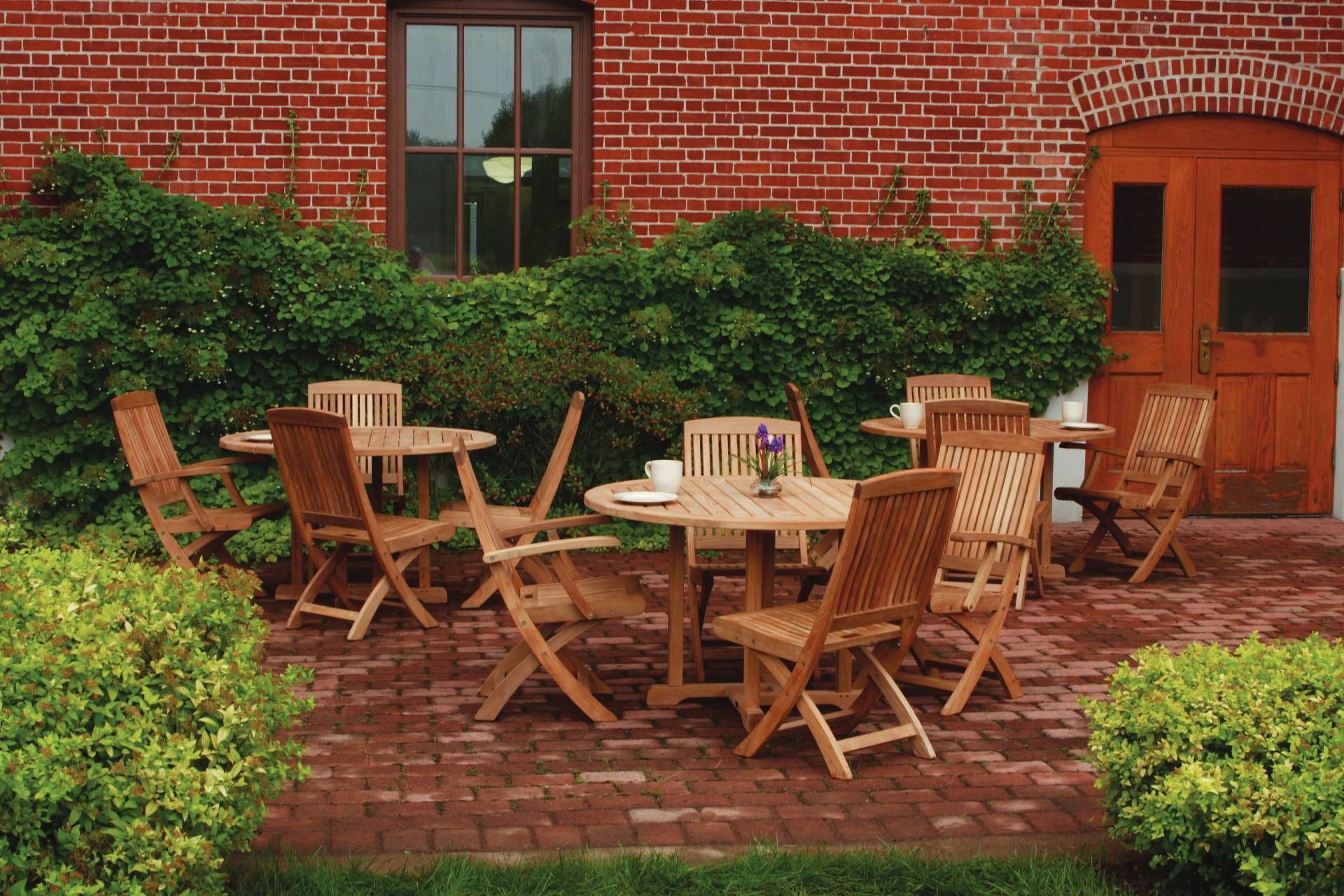 Outdoor wooden tables and chairs on a brick patio in front of a brick building.
