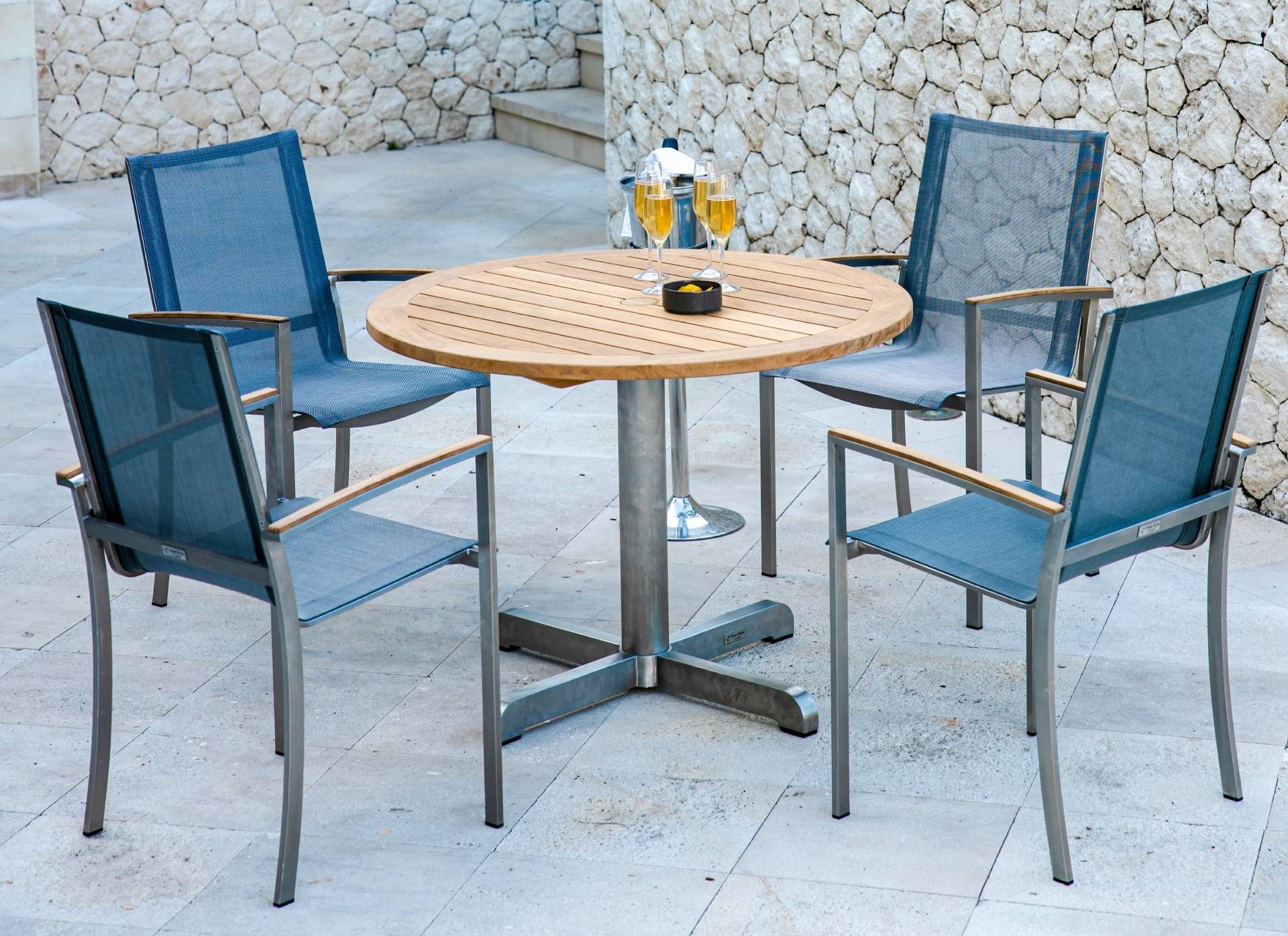 Outdoor table and chairs set on a patio. Four blue mesh chairs surround a wooden round table.