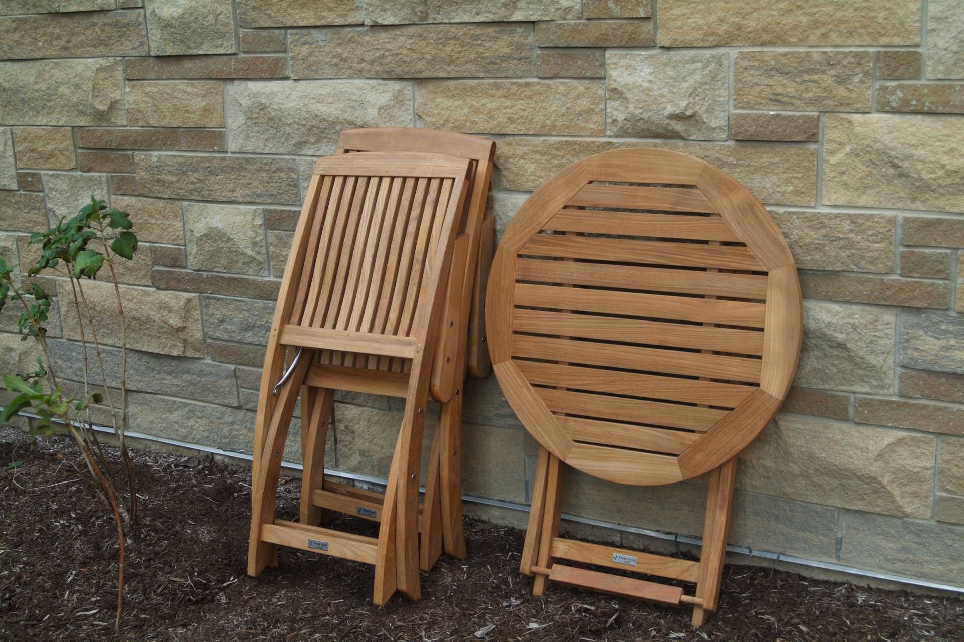 Folded wooden patio chair and table against a stone wall.