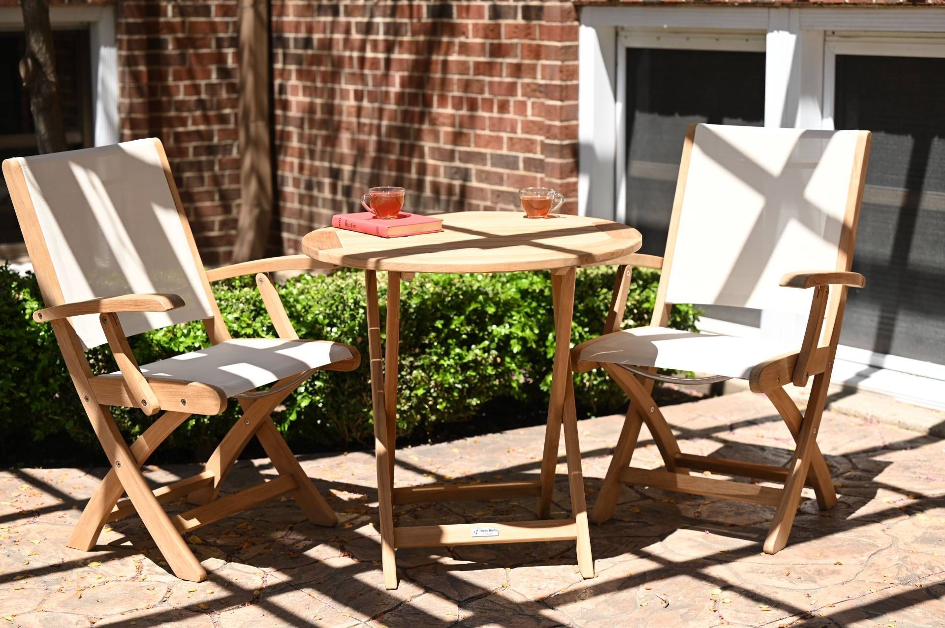 Two wooden folding chairs and a small table on a patio. Beverages are on the table.