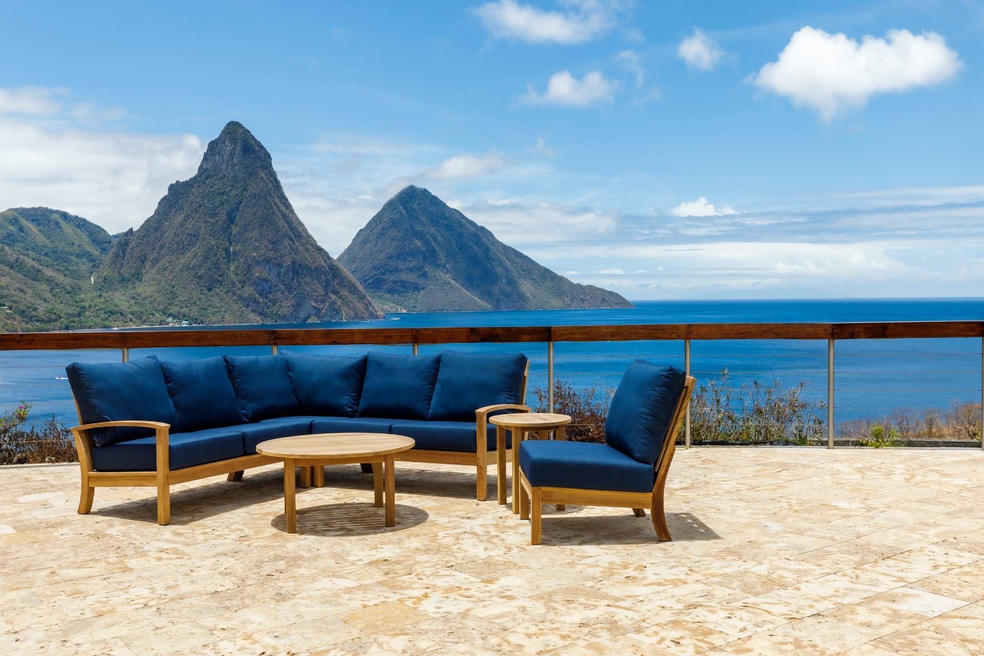 Outdoor sectional seating with blue cushions, coffee table, and armchair on a patio overlooking ocean and mountains.