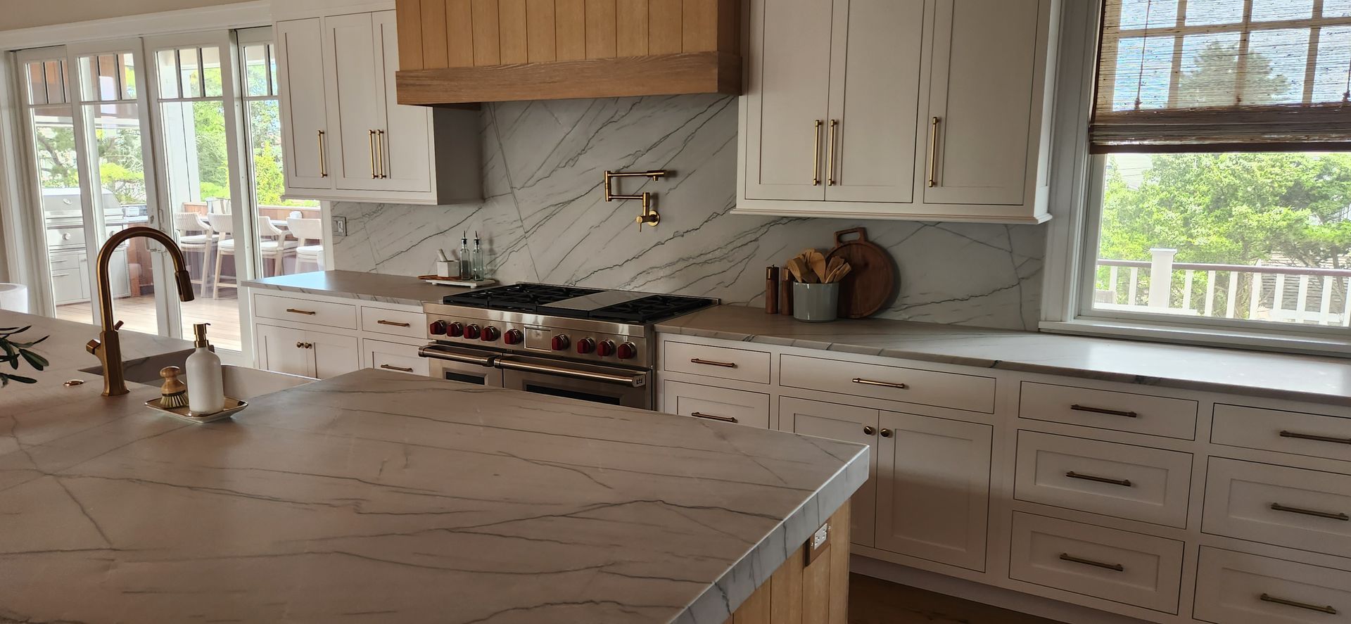 A modern kitchen with white cabinets, light countertops, and a wooden range hood.