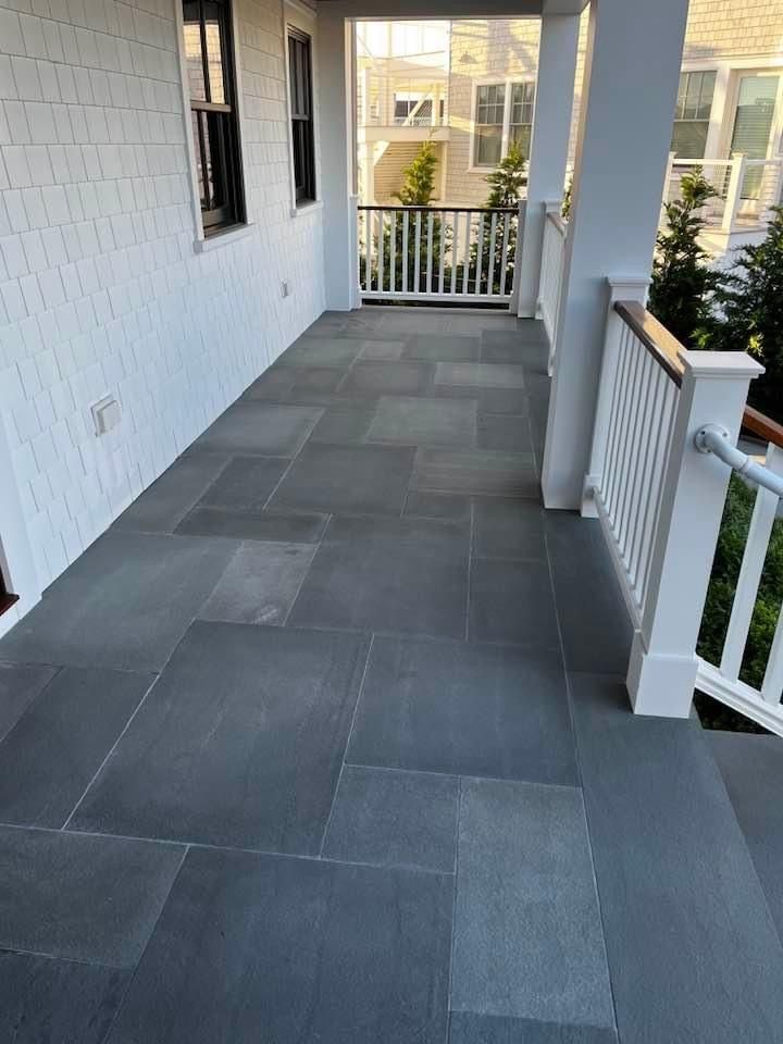 Gray stone tile porch with white railing and siding.